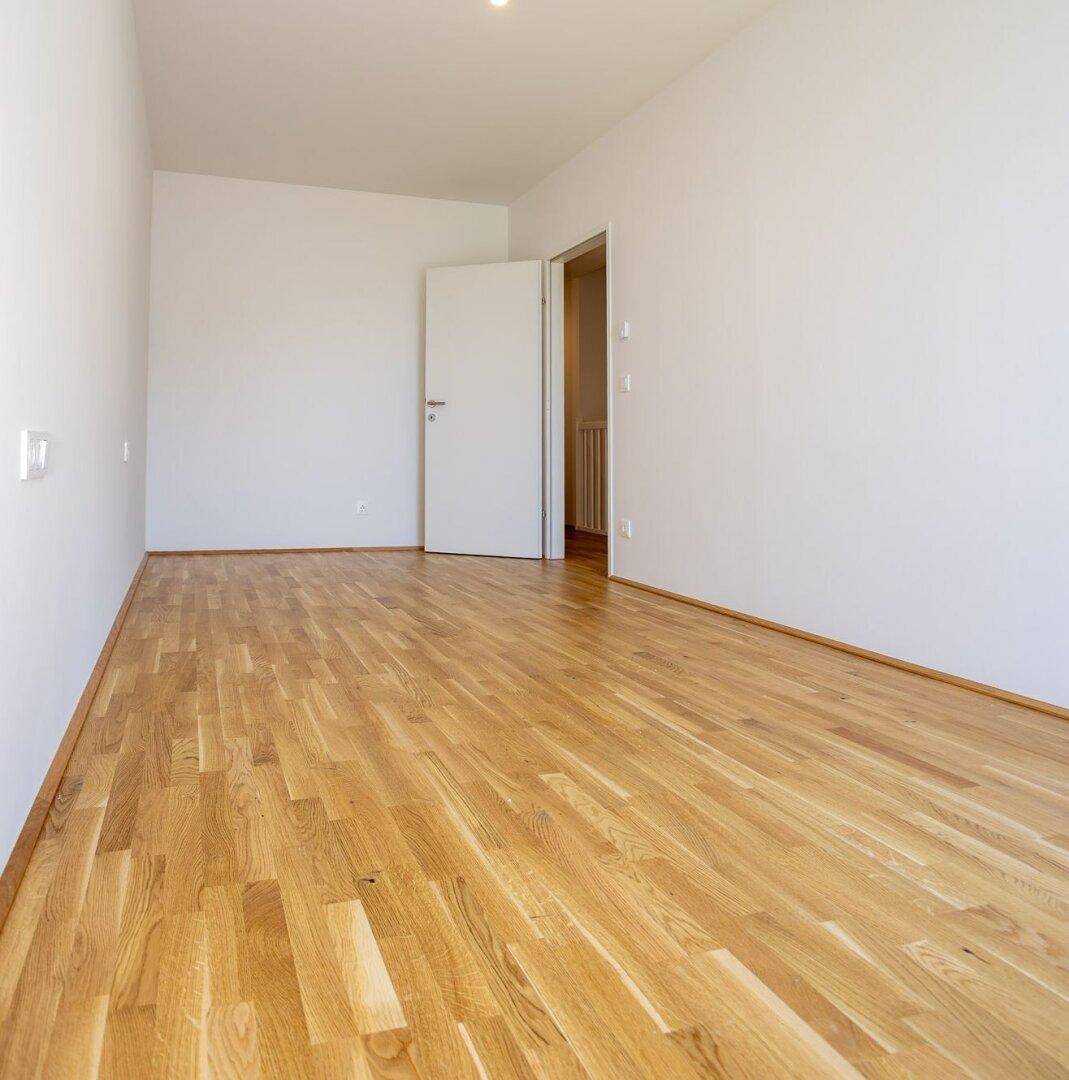 Leeres Zimmer mit Eichenparkettboden und weiß gestrichenen Wänden.