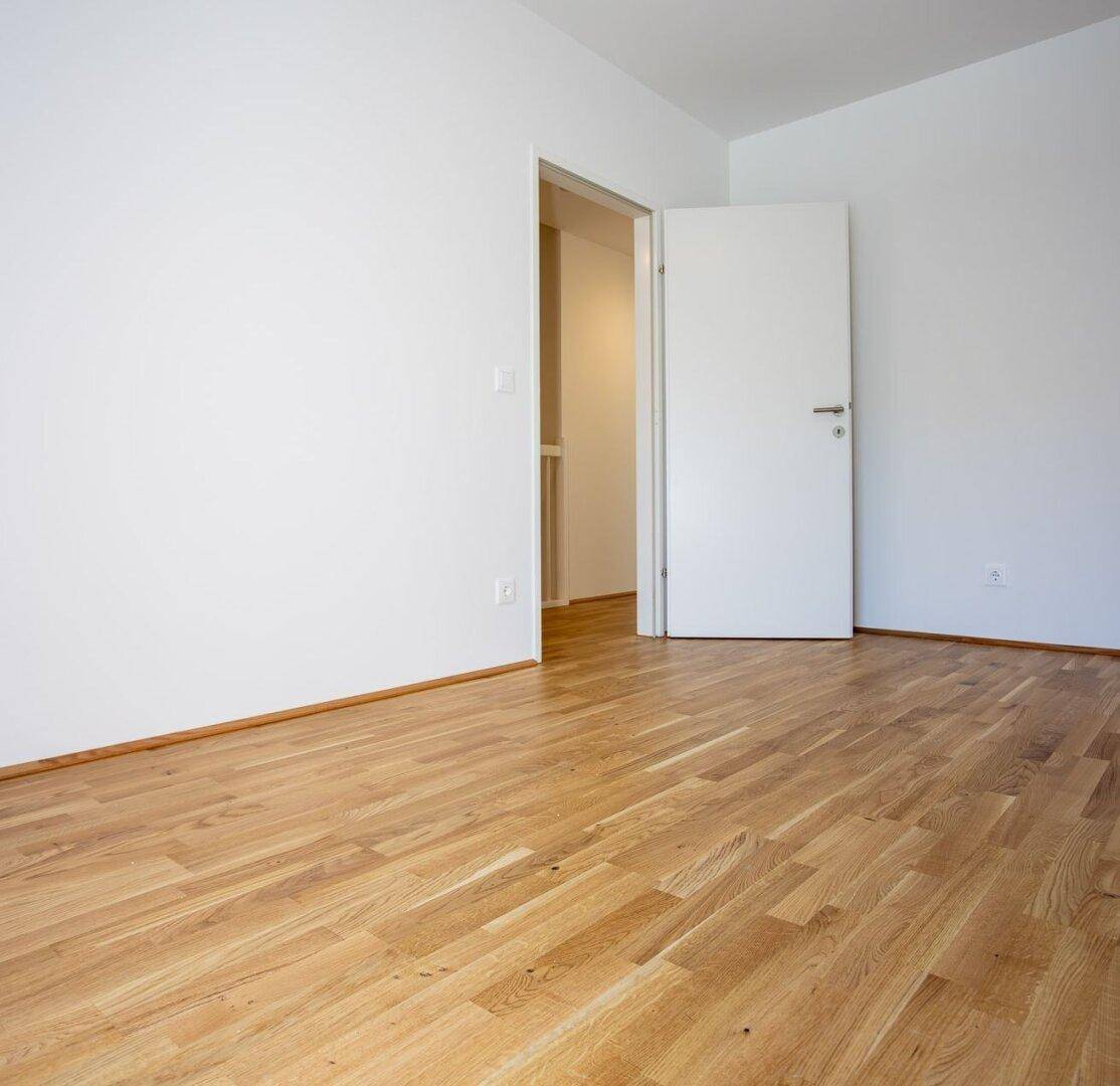 Leeres Zimmer mit Eichenparkettboden und Zugang zum Flur.