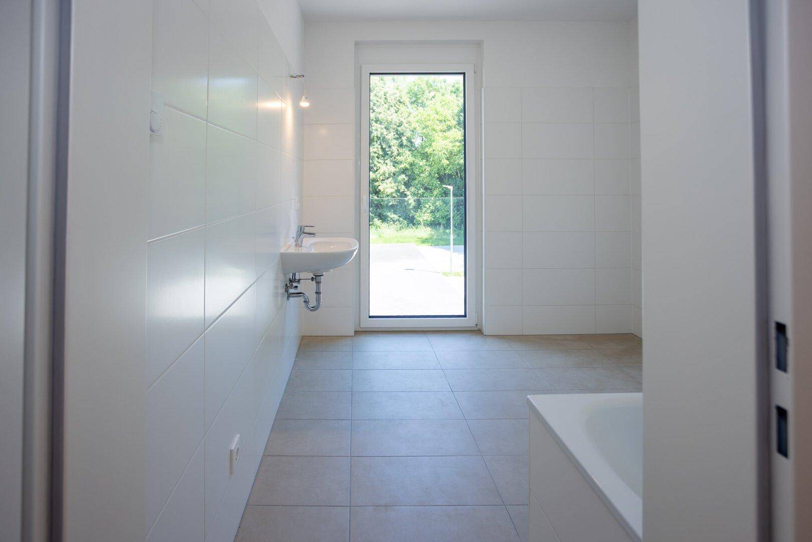 Modernes Badezimmer mit weißen Fliesen, Waschbecken und großem Fenster.
