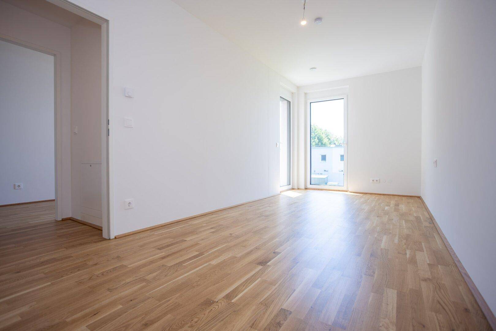 Helles Zimmer mit Eichenparkettboden und Fenster mit Blick ins Grüne.