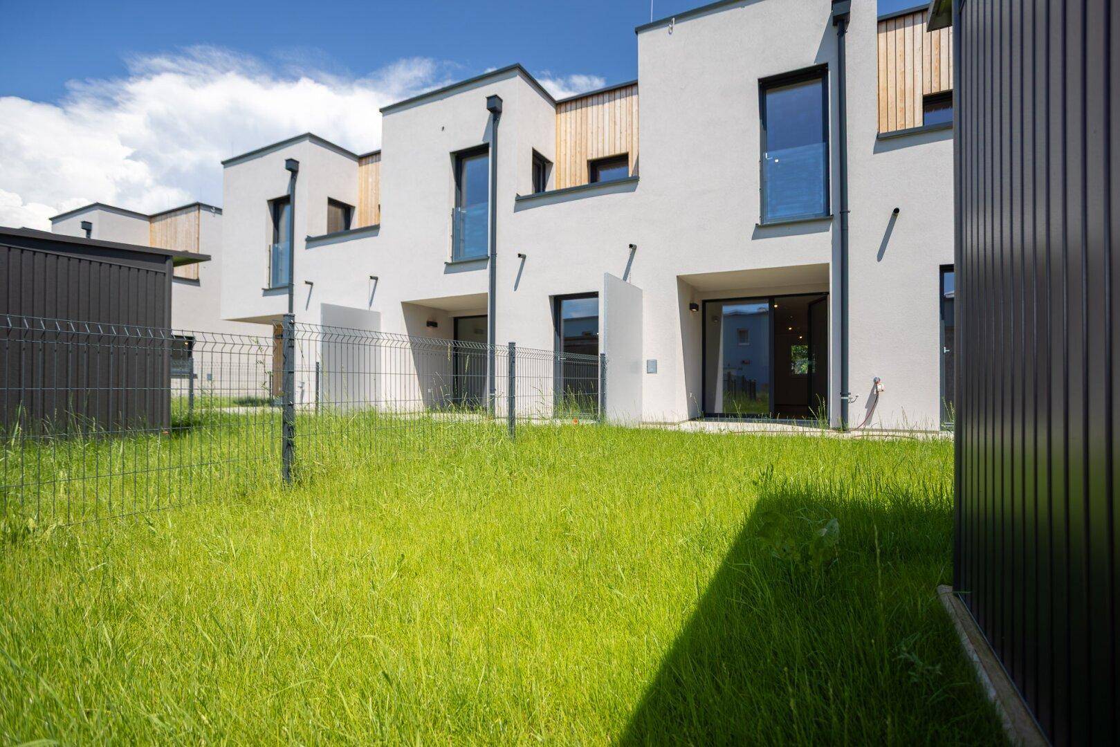 Reihenhäuser mit gepflegtem Rasen und moderner Architektur unter blauem Himmel.