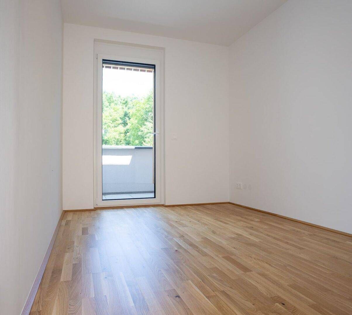 Helles Schlafzimmer mit Eichenparkett, weißen Wänden und Zugang zu einem kleinen Balkon.