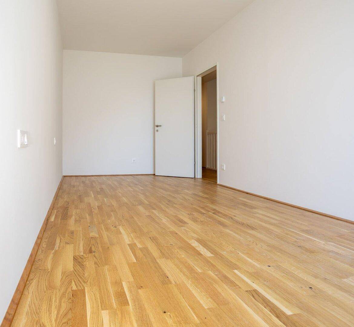Helles Zimmer mit Eichenparkett und weiß gestrichenen Wänden, ideal als Schlaf- oder Arbeitszimmer.