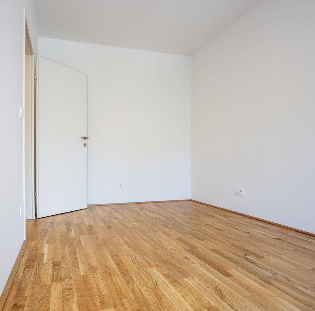 Leeres Zimmer mit Eichenparkett und weißen Wänden, bereit zur individuellen Gestaltung.