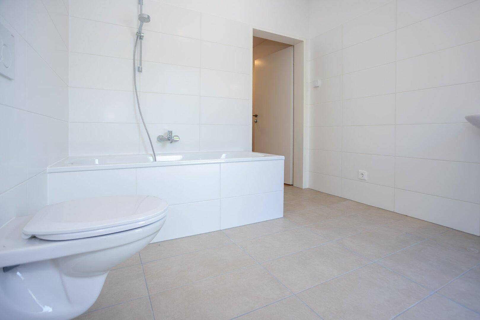 Modernes Badezimmer mit weißen Fliesen, Badewanne und wandhängendem WC.