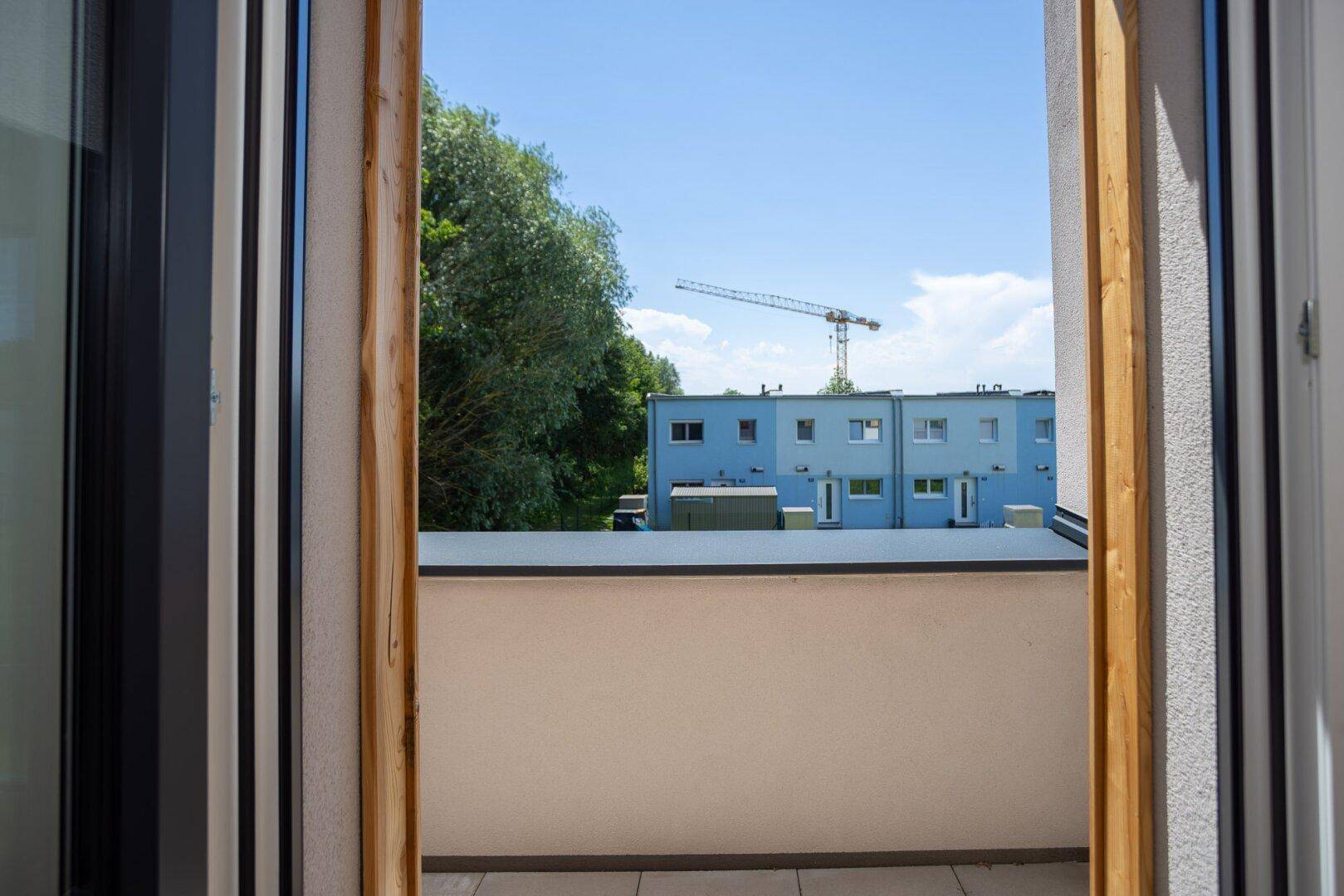 Blick vom Innenraum durch die Balkontür auf einen Baukran und ein blaues Gebäude.