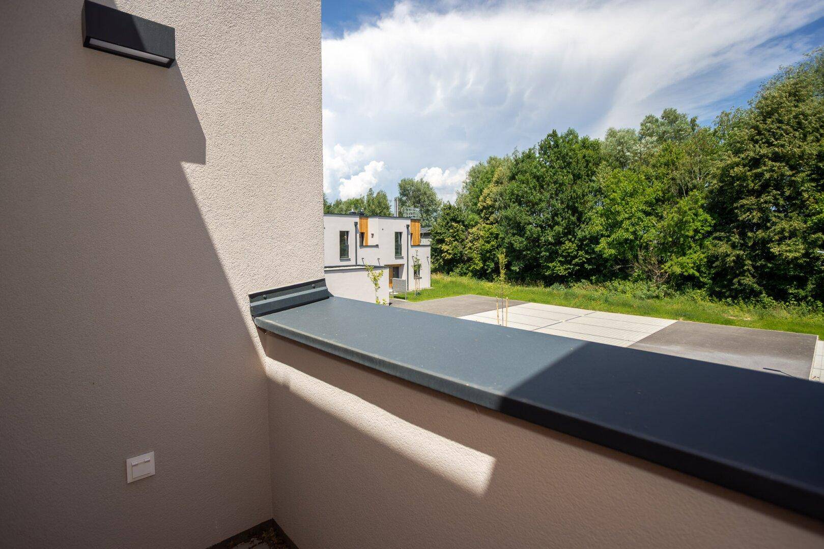 Balkonaussicht auf die Umgebung mit weiteren Gebäuden und viel Grün in der Ferne.