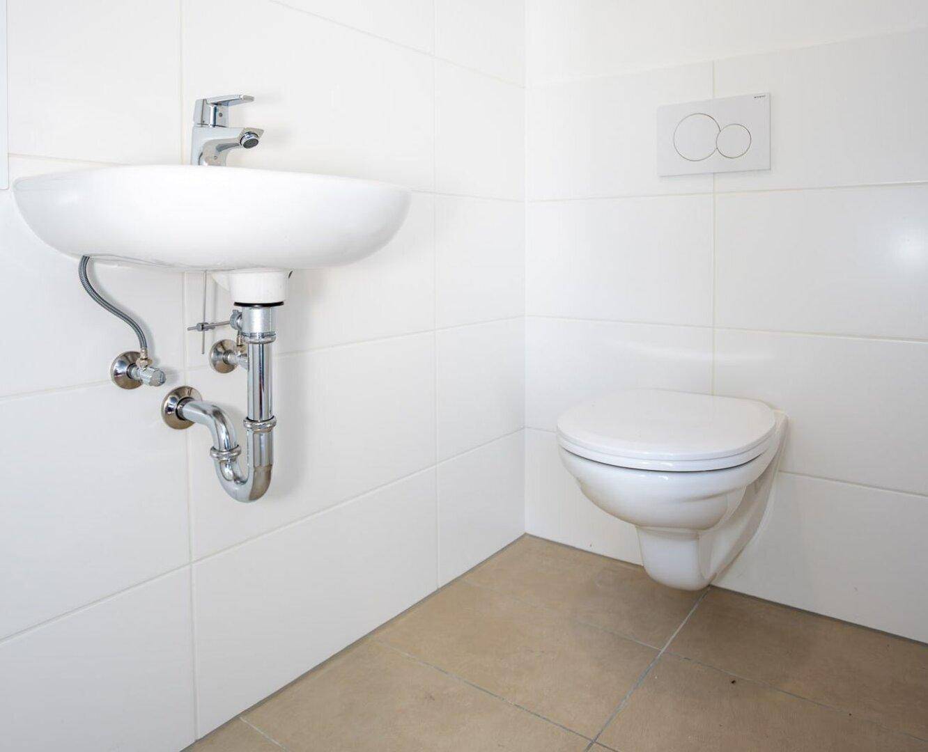 Waschbecken und wandhängendes WC in einem modern gefliesten Badezimmer mit weißen Fliesen.