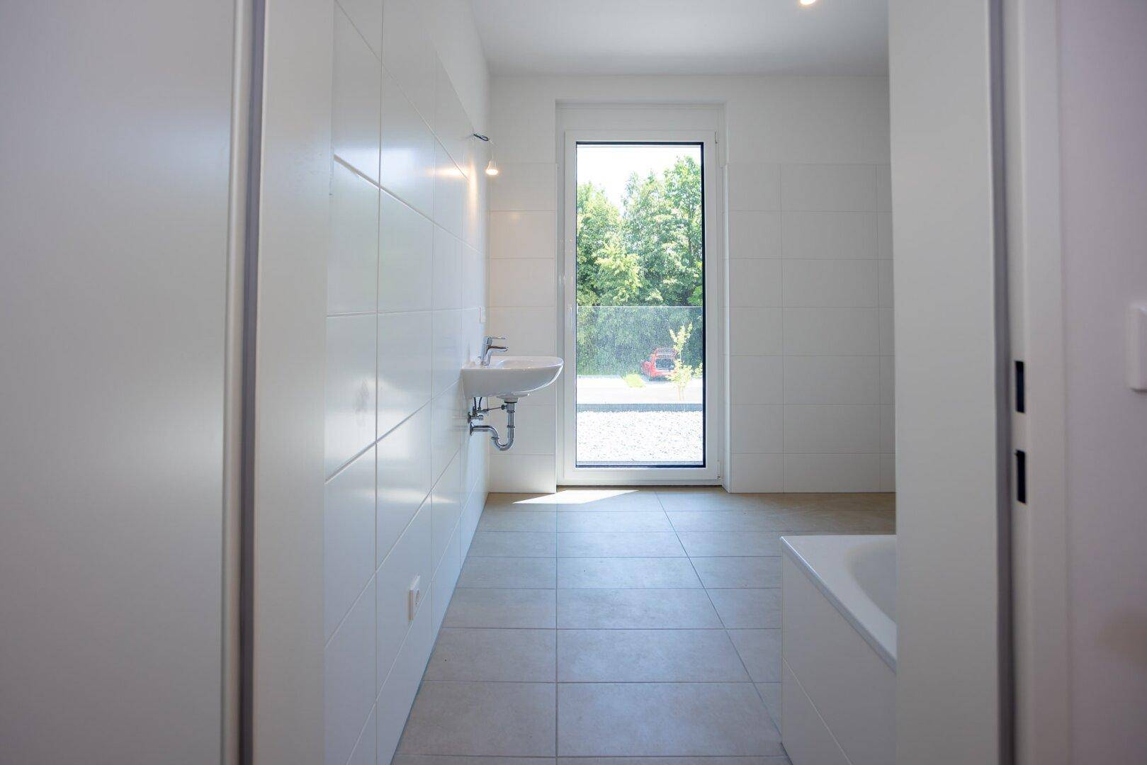 Modernes Badezimmer mit weißen Fliesen, hellem Boden und einem großen Fenster mit Ausblick.