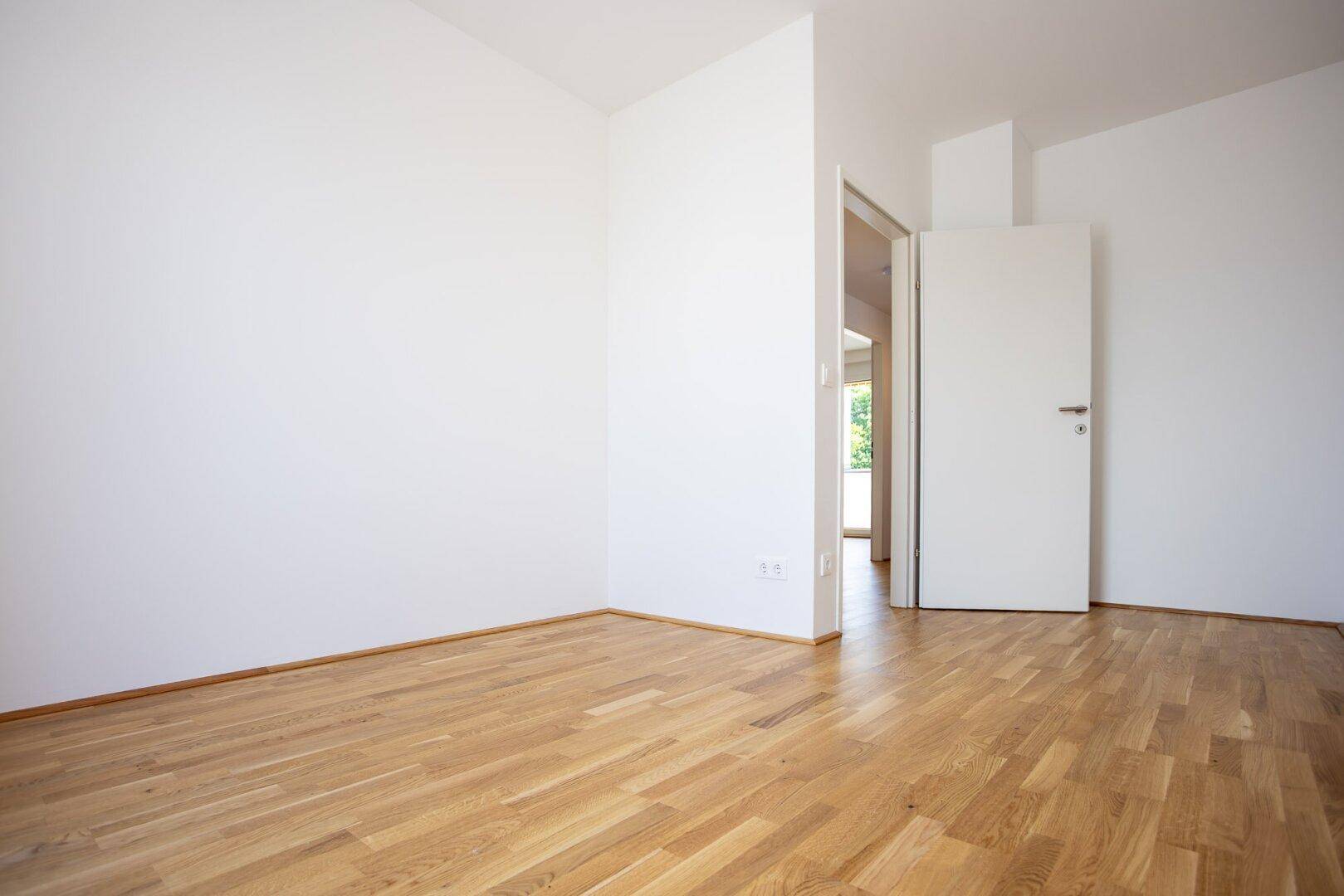 Leeres Zimmer mit hellem Parkettboden und weißen Wänden, bereit zur individuellen Gestaltung.
