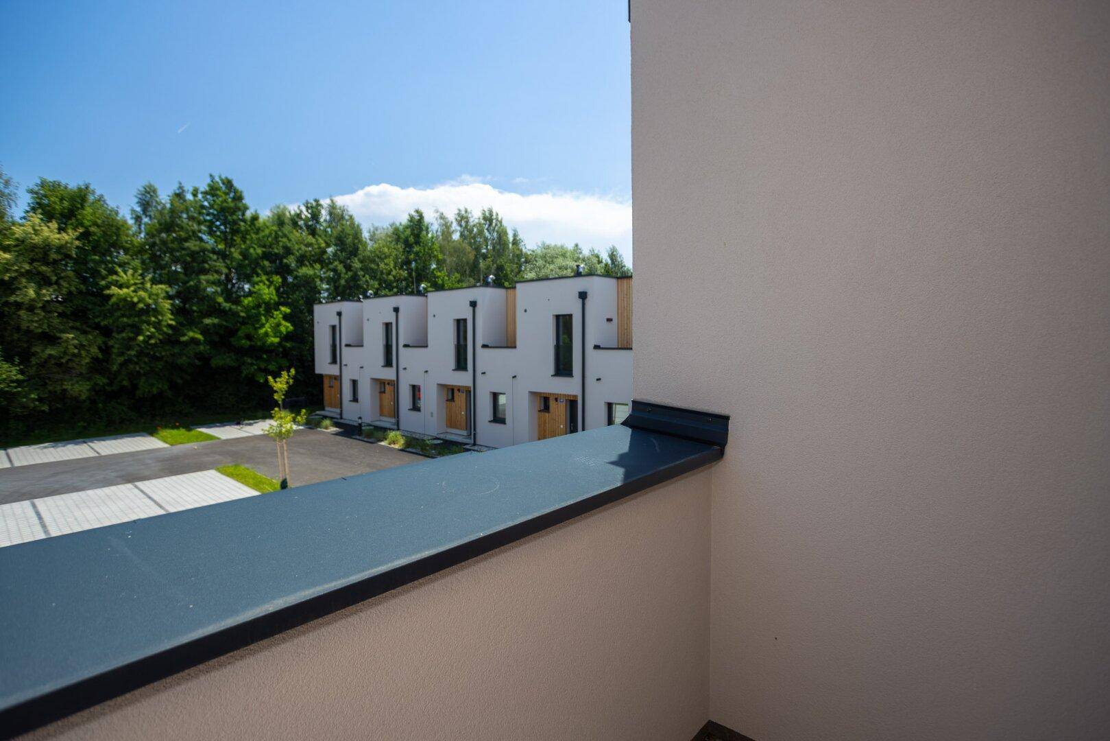 Blick vom Balkon auf weitere moderne Reihenhäuser und einen gepflasterten Parkbereich.