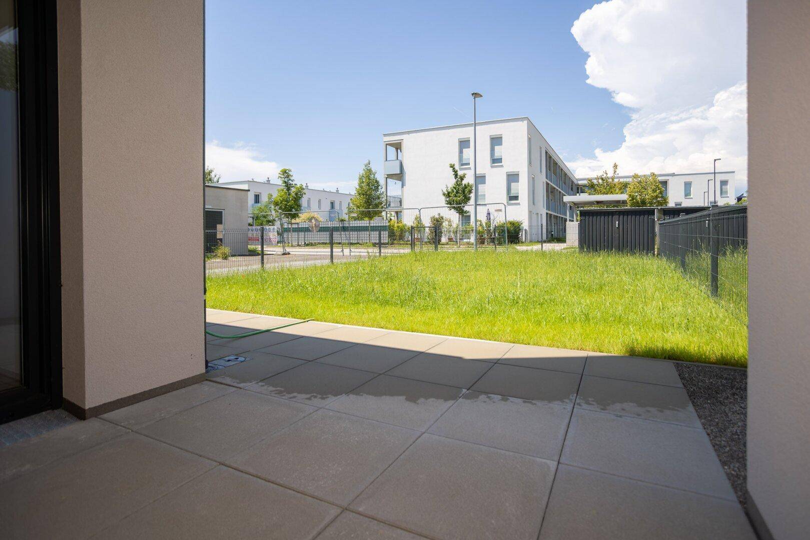 Gepflasterte Terrasse mit Blick auf eine grüne Rasenfläche und moderne Wohngebäude.