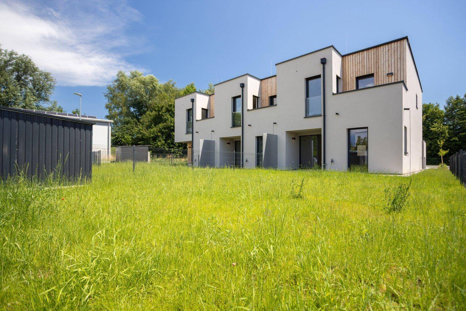 Moderne Reihenhäuser mit weißen Fassaden, Holzelementen und privaten Grünflächen.
