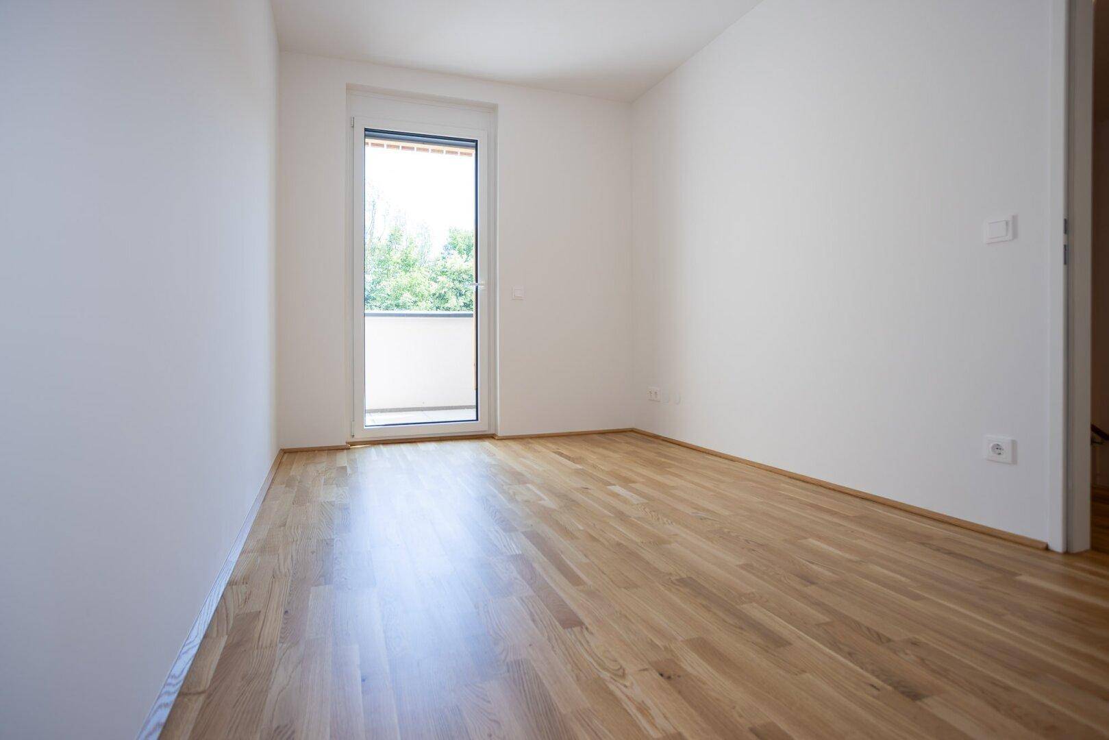Helles Schlafzimmer mit Parkettboden, weißen Wänden und einem französischen Balkon.