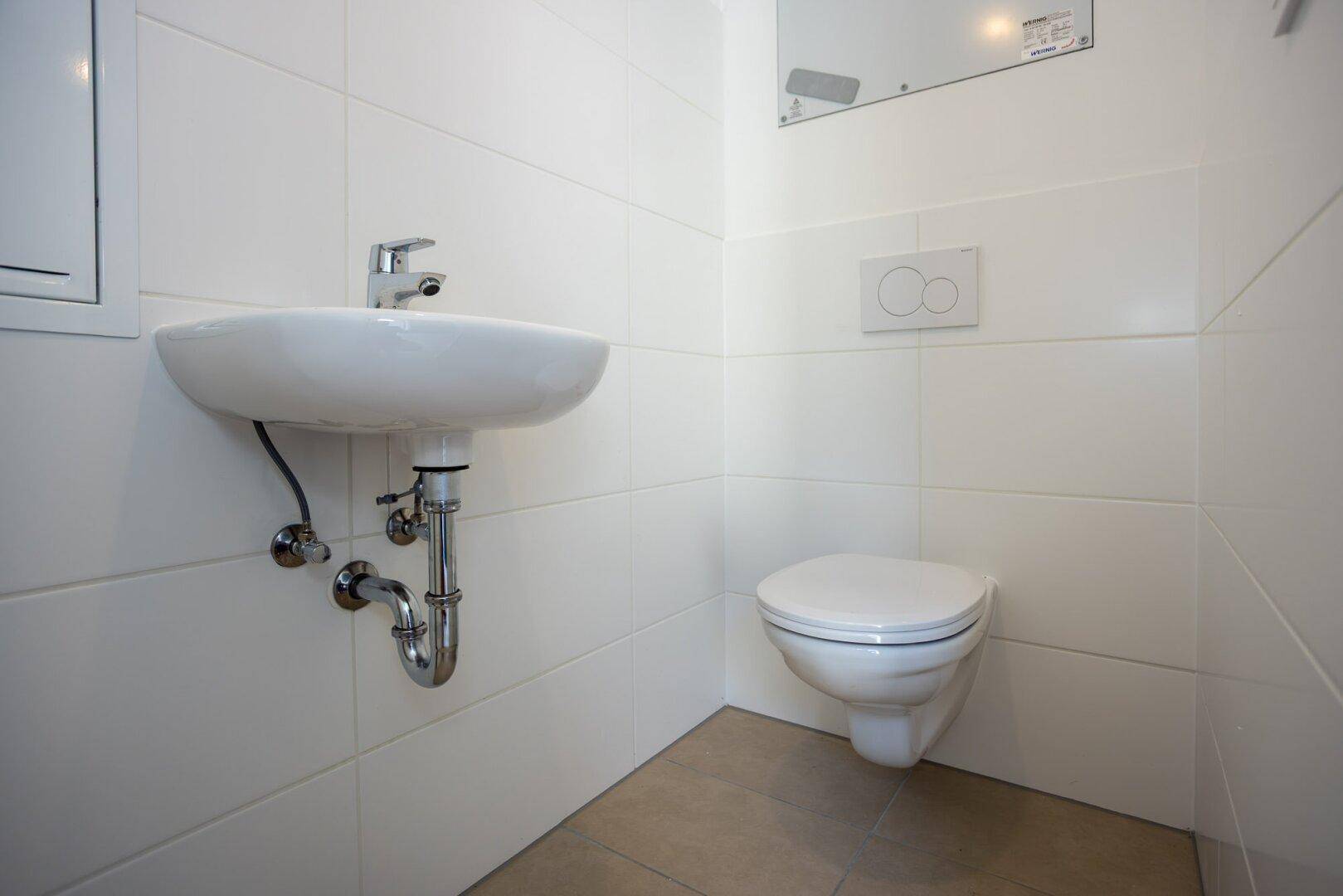Modernes Gäste-WC mit Waschbecken und wandhängender Toilette, ausgestattet mit hellen Fliesen.