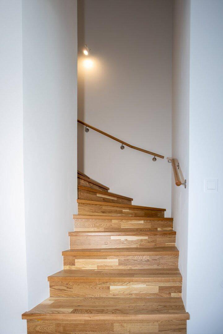 Eine moderne Holztreppe mit schlichtem Geländer führt in die obere Etage des Hauses.
