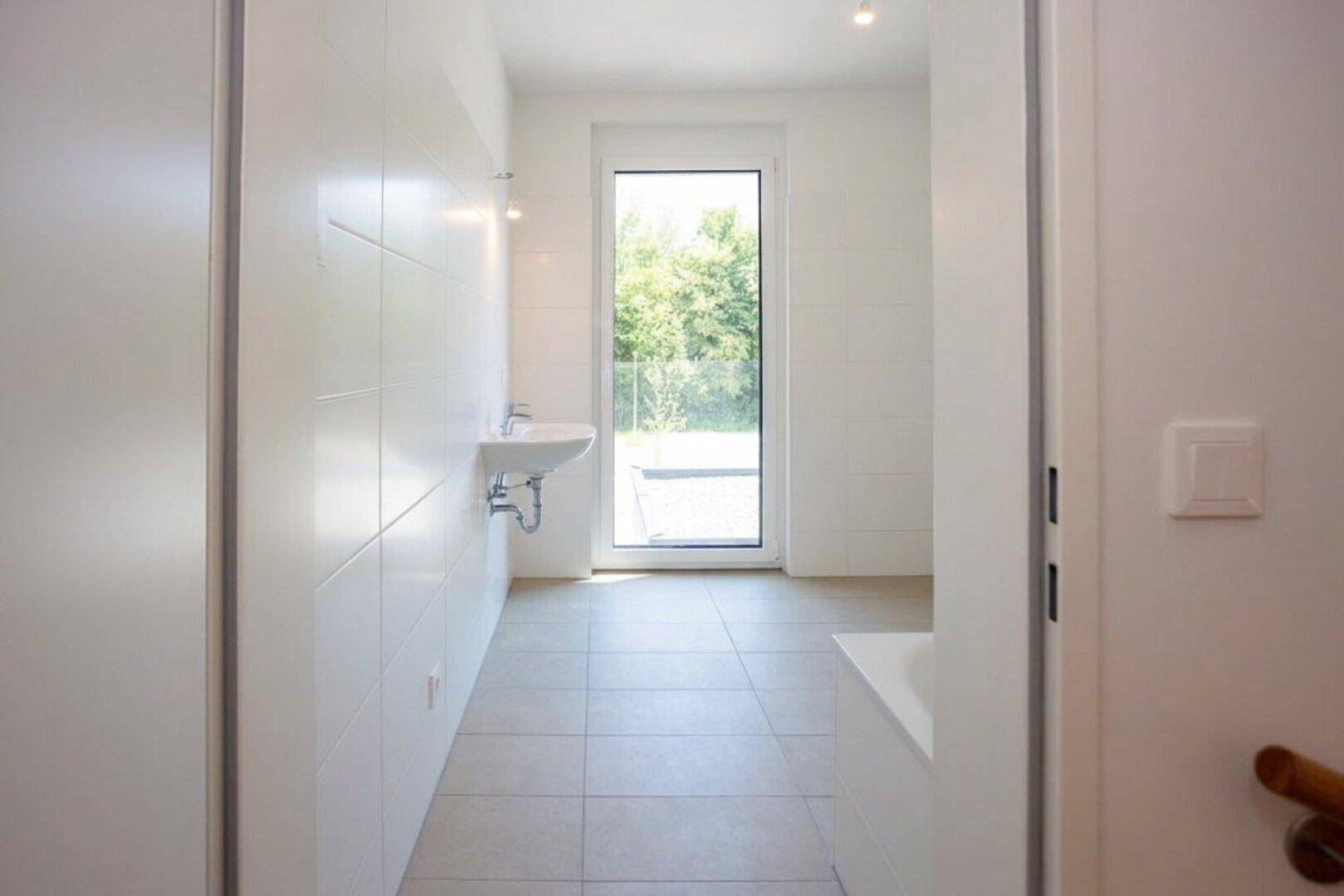 Modernes Badezimmer mit hellen Fliesen, einem Waschbecken und einem großen Fenster.