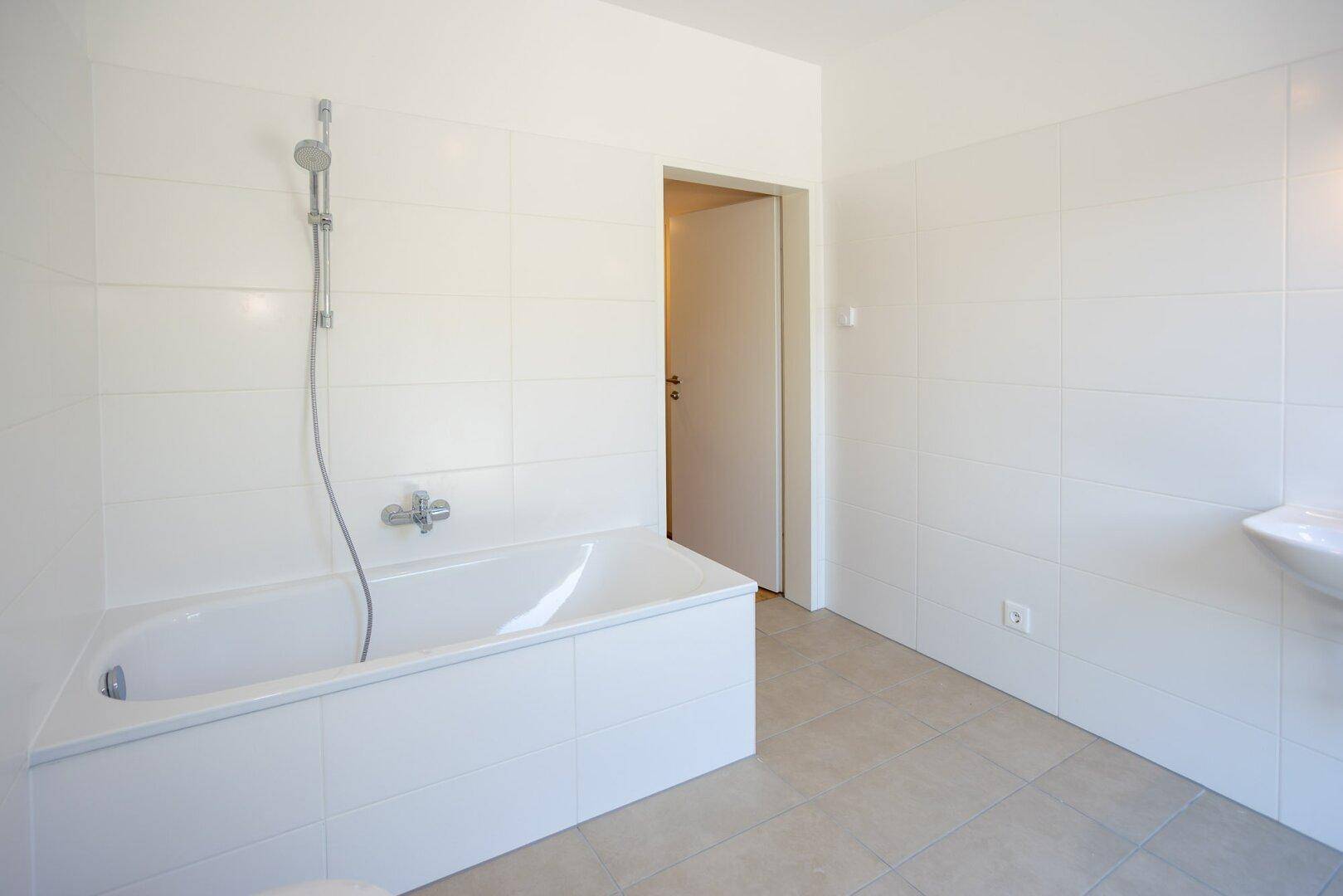 Modernes Badezimmer mit Badewanne und Duscharmatur, hellen Fliesen und viel Platz.