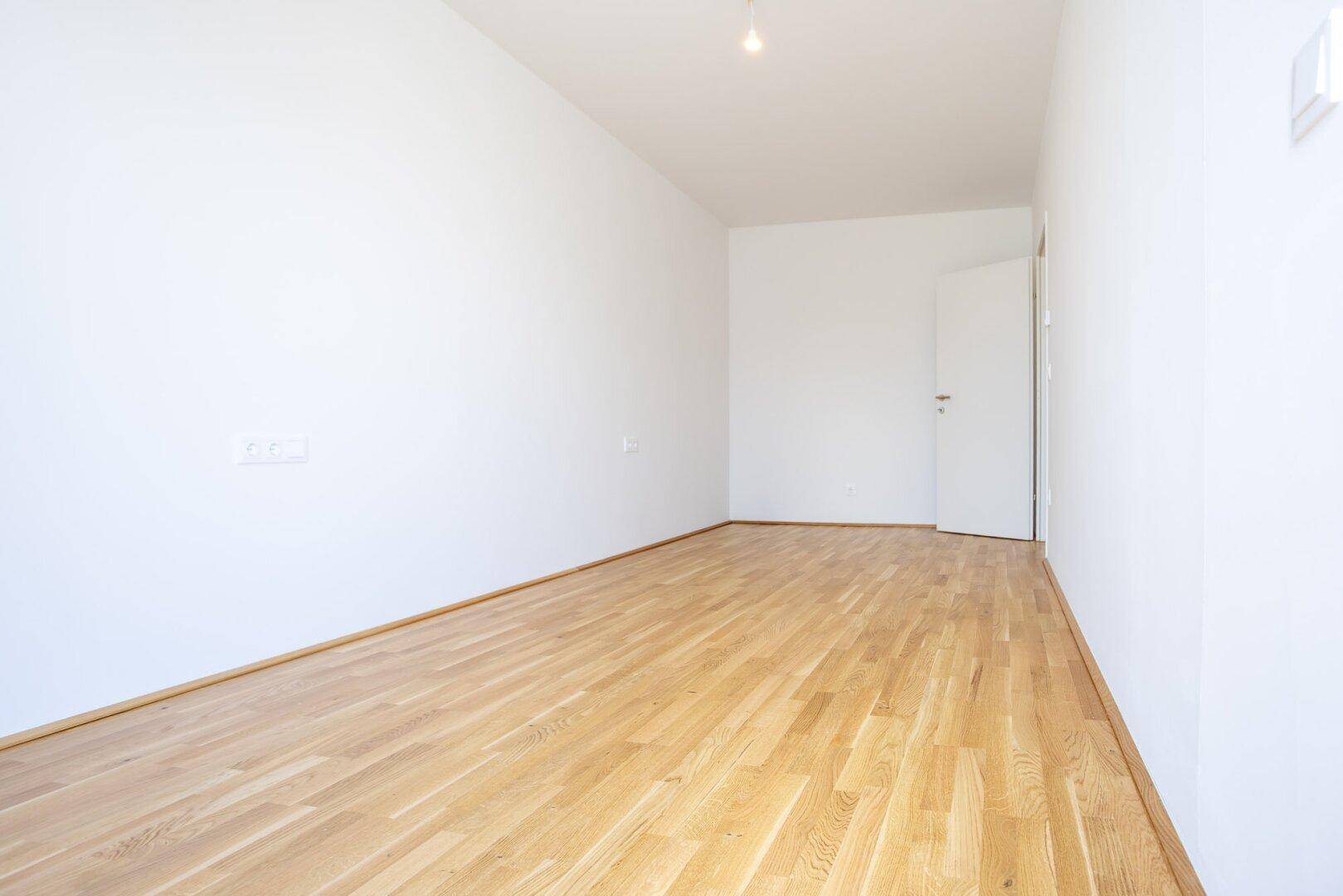 Helles und geräumiges Schlafzimmer mit Parkettboden und weißen Wänden, ideal für Ruhe und Entspannung.