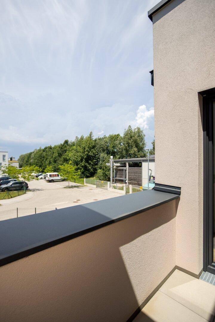 Blick vom Balkon auf die Umgebung mit Bäumen und einem Parkplatz unter blauem Himmel.
