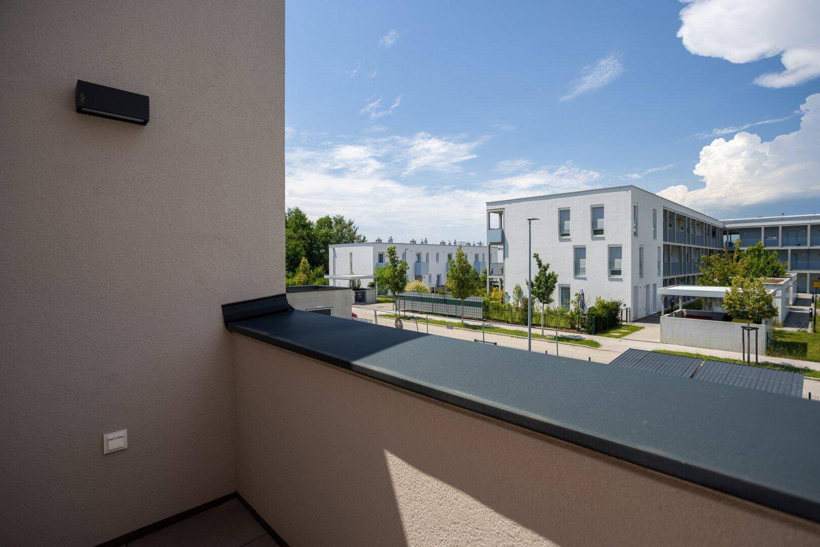 Balkon mit Blick auf die Wohnanlage und die umliegenden Gebäude unter einem sonnigen Himmel.