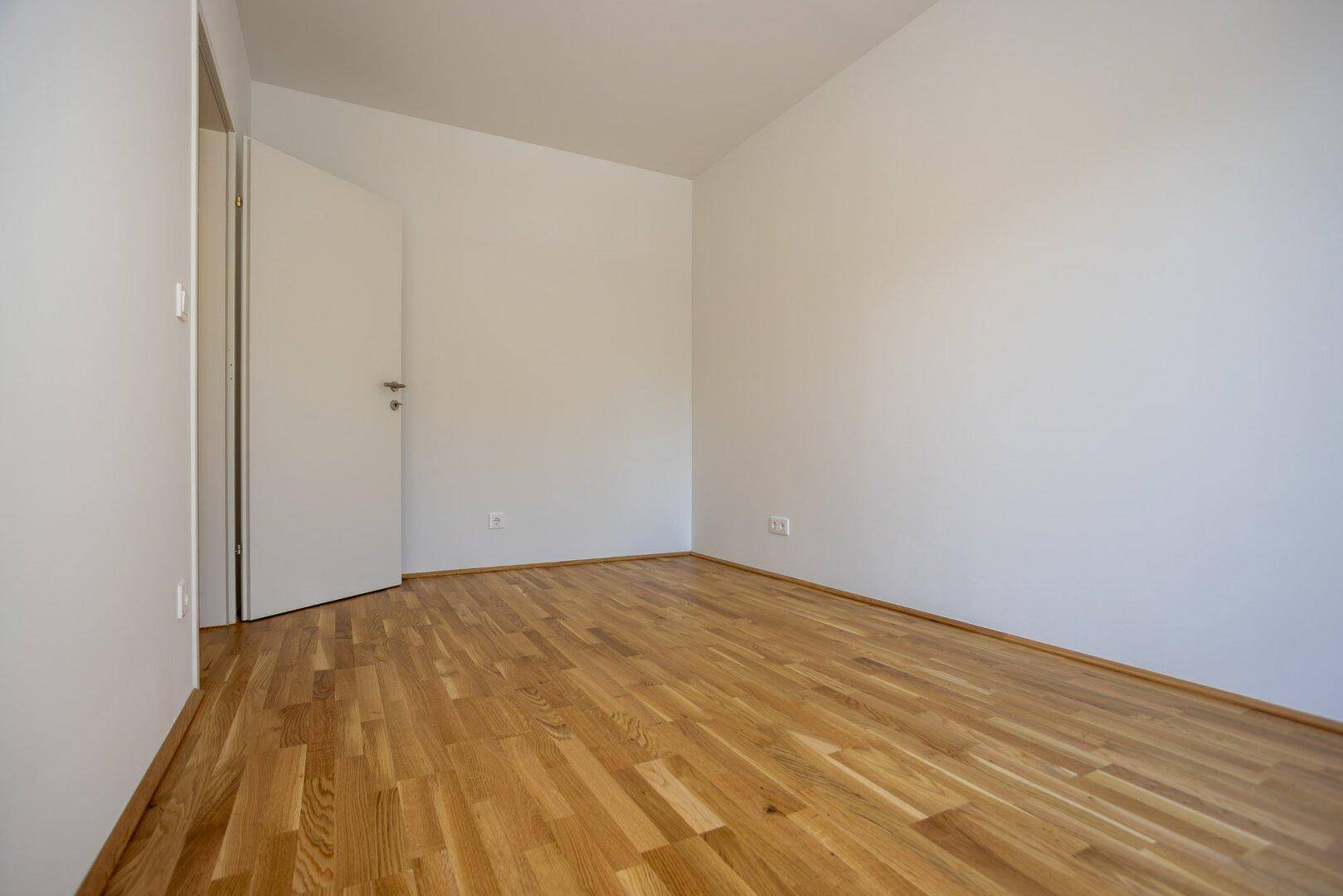 Leeres Schlafzimmer mit hellem Parkettboden und weißen Wänden, bereit zur individuellen Gestaltung.