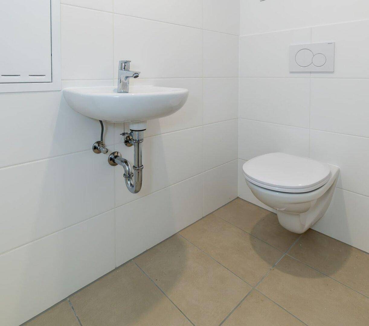 Kleines, hell gefliestes Gäste-WC mit wandhängendem WC und Waschbecken.