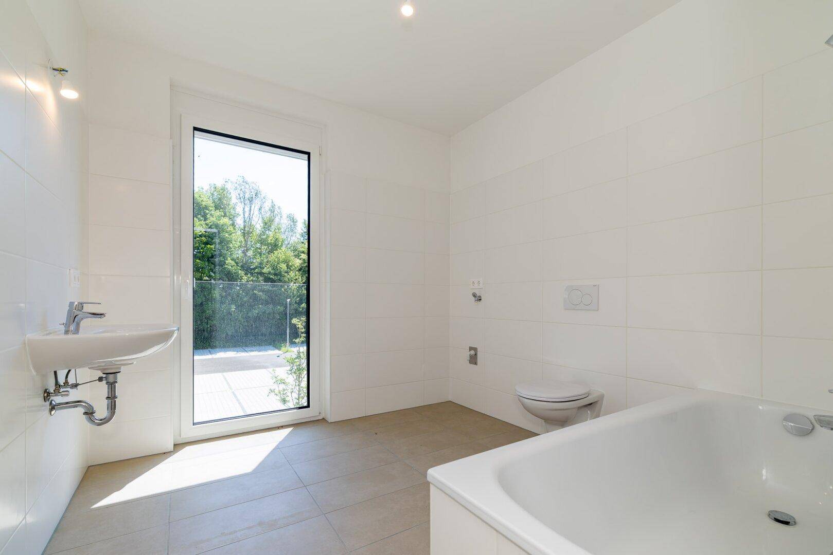 Modernes Badezimmer mit Badewanne, wandhängendem WC und Waschbecken, hell gefliest.