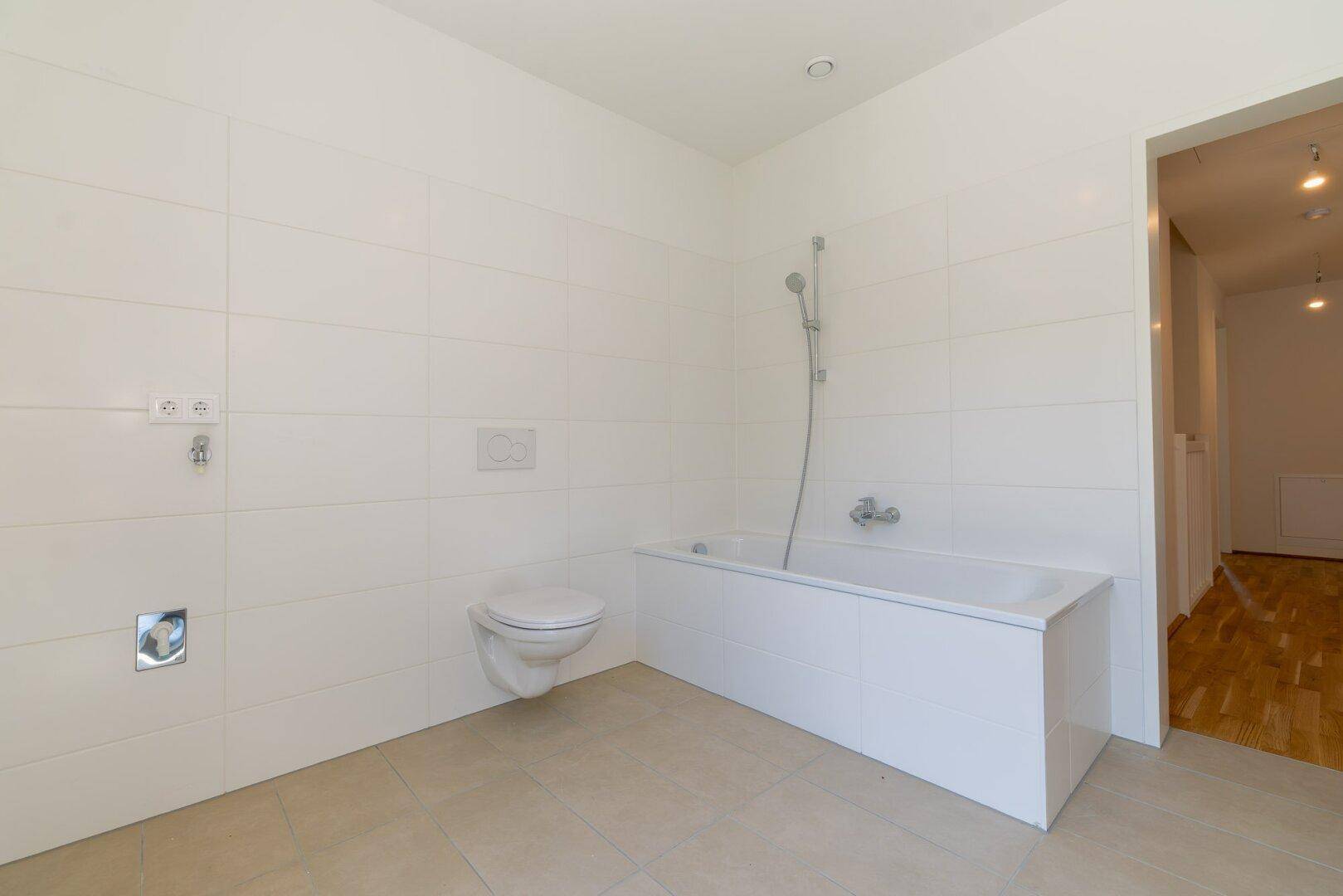 Helles Badezimmer mit Badewanne und wandhängendem WC, weiß gefliest und modern.