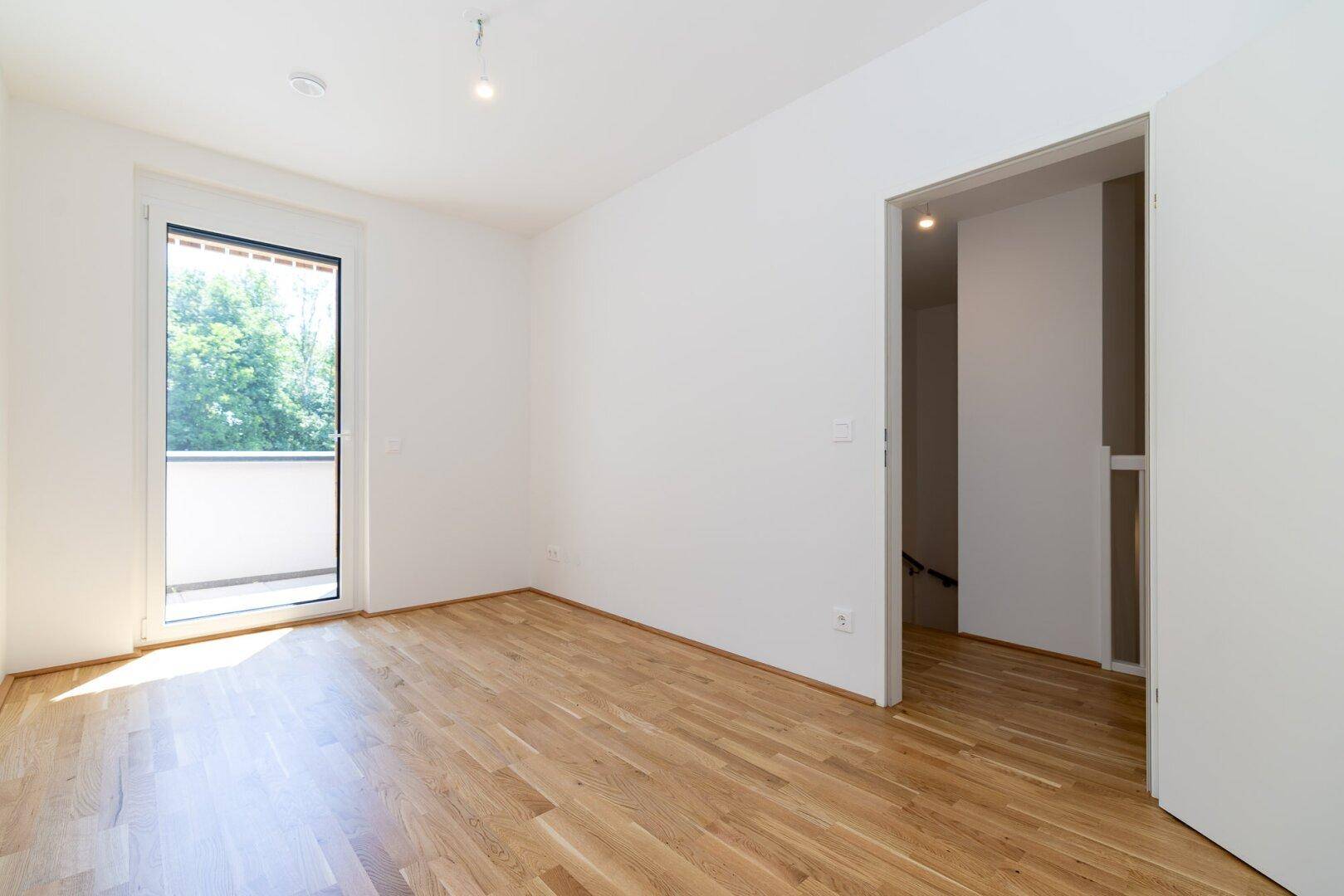 Helles Schlafzimmer mit Parkettboden und Zugang zu einem kleinen Balkon.