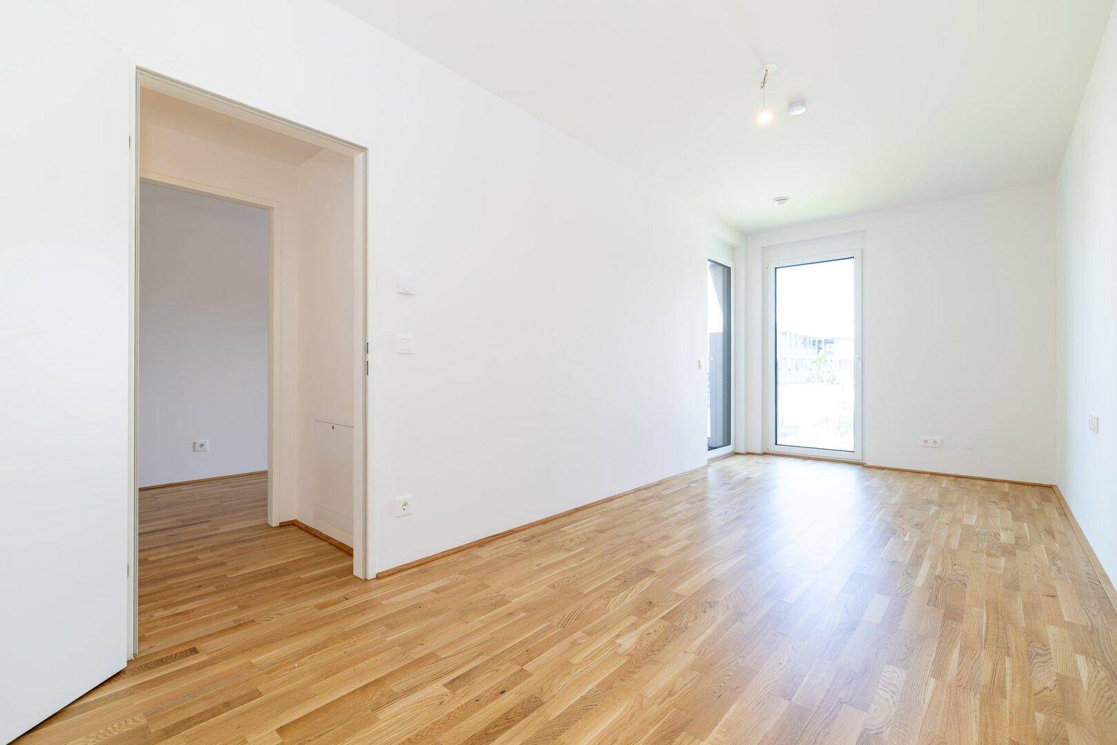 Geräumiges, helles Zimmer mit Parkettboden und Zugang zu einem Balkon.