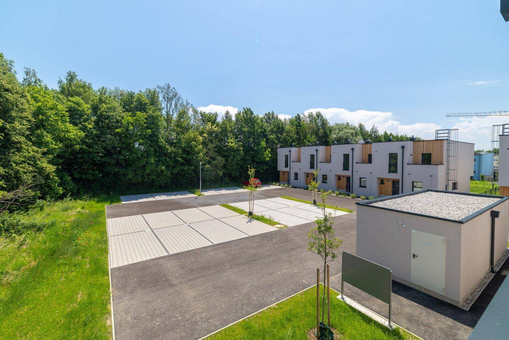 Weitläufiger Außenbereich mit Parkplätzen und mehreren modernen Reihenhäusern, umgeben von Grün.