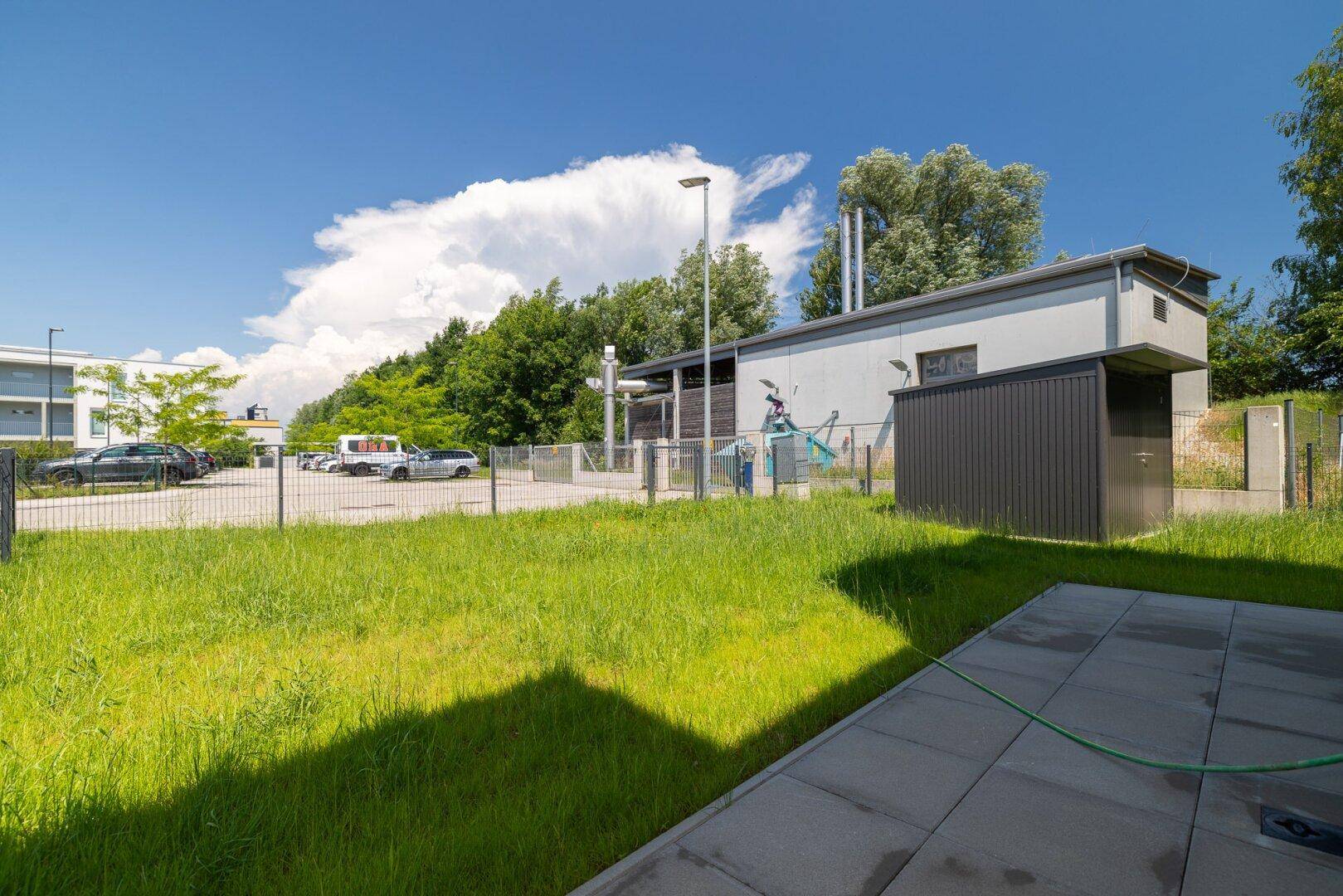 Außenbereich mit einem Nebengebäude, Parkplätzen und einer Grünfläche unter blauem Himmel.