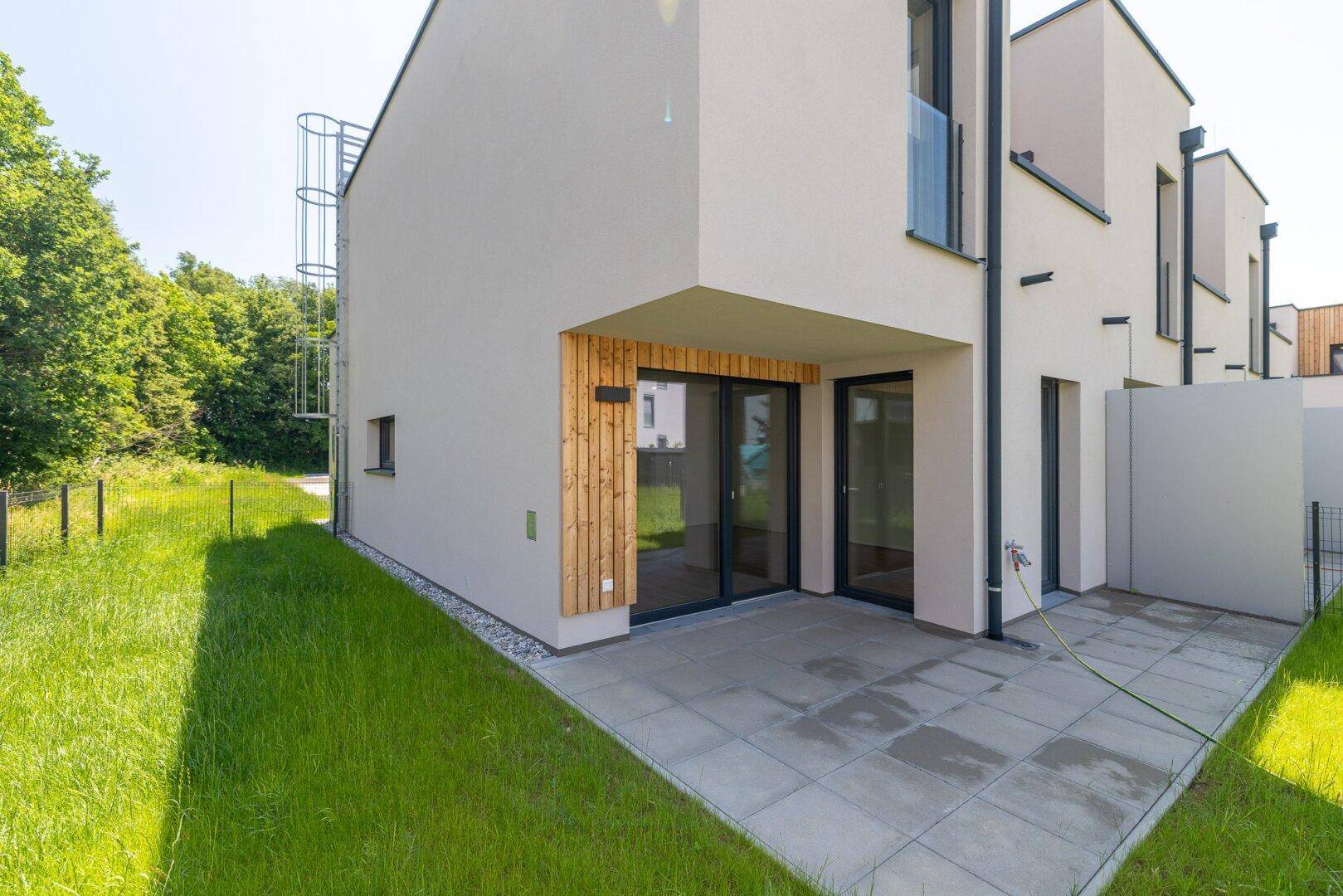 Moderne Terrasse mit Steinplatten und Zugang zum Garten, angrenzend an ein Reihenhaus.