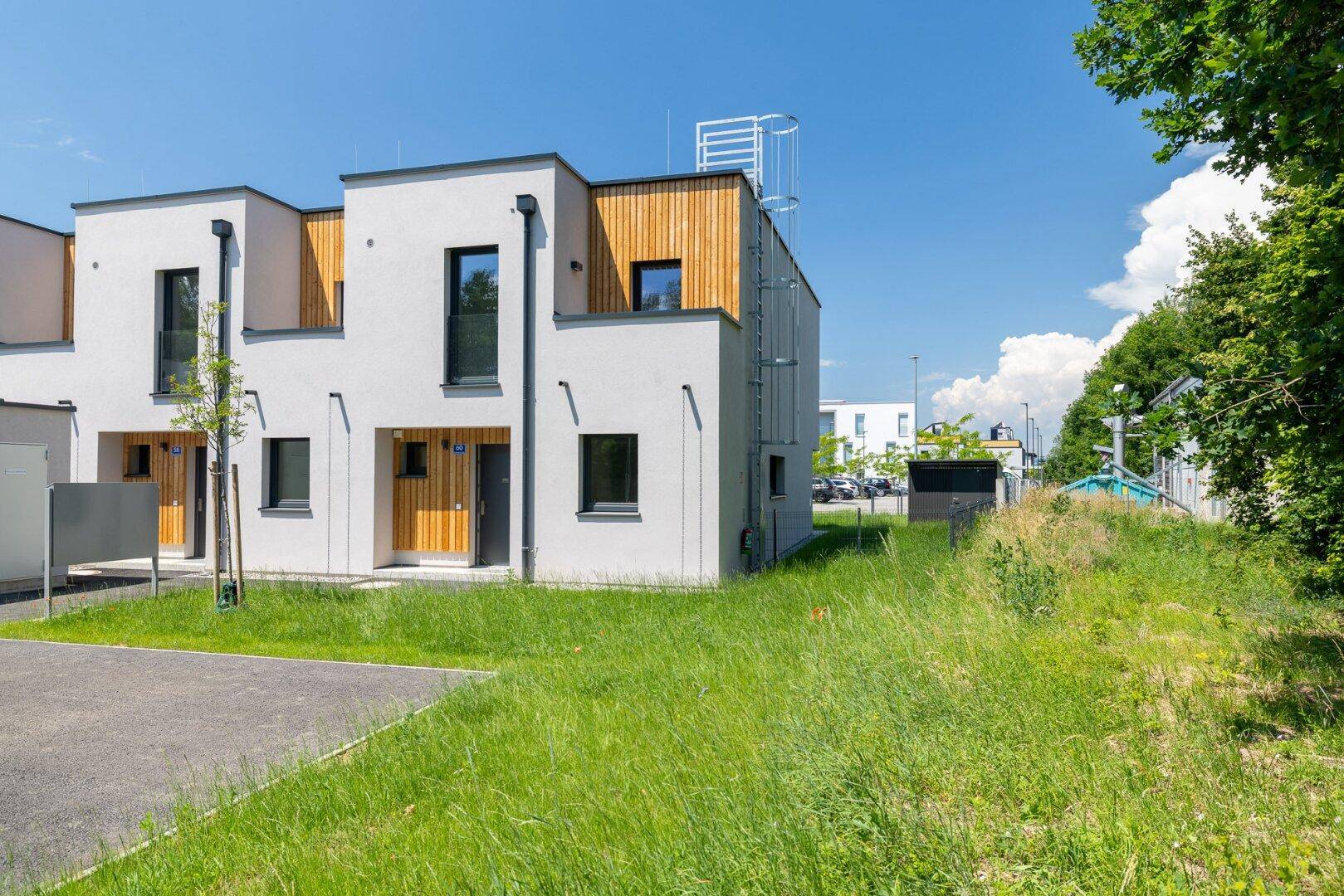 Reihe moderner Reihenhäuser mit weißer Fassade und Holzdetails, umgeben von Grünflächen.