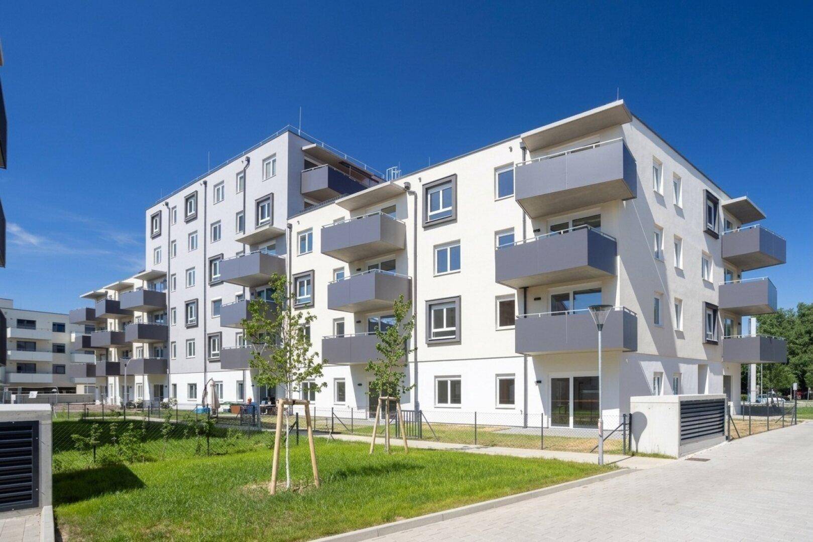 Modernes Mehrfamilienhaus mit hellen Fassaden, Balkonen und gepflegten Grünflächen unter blauem Himmel.