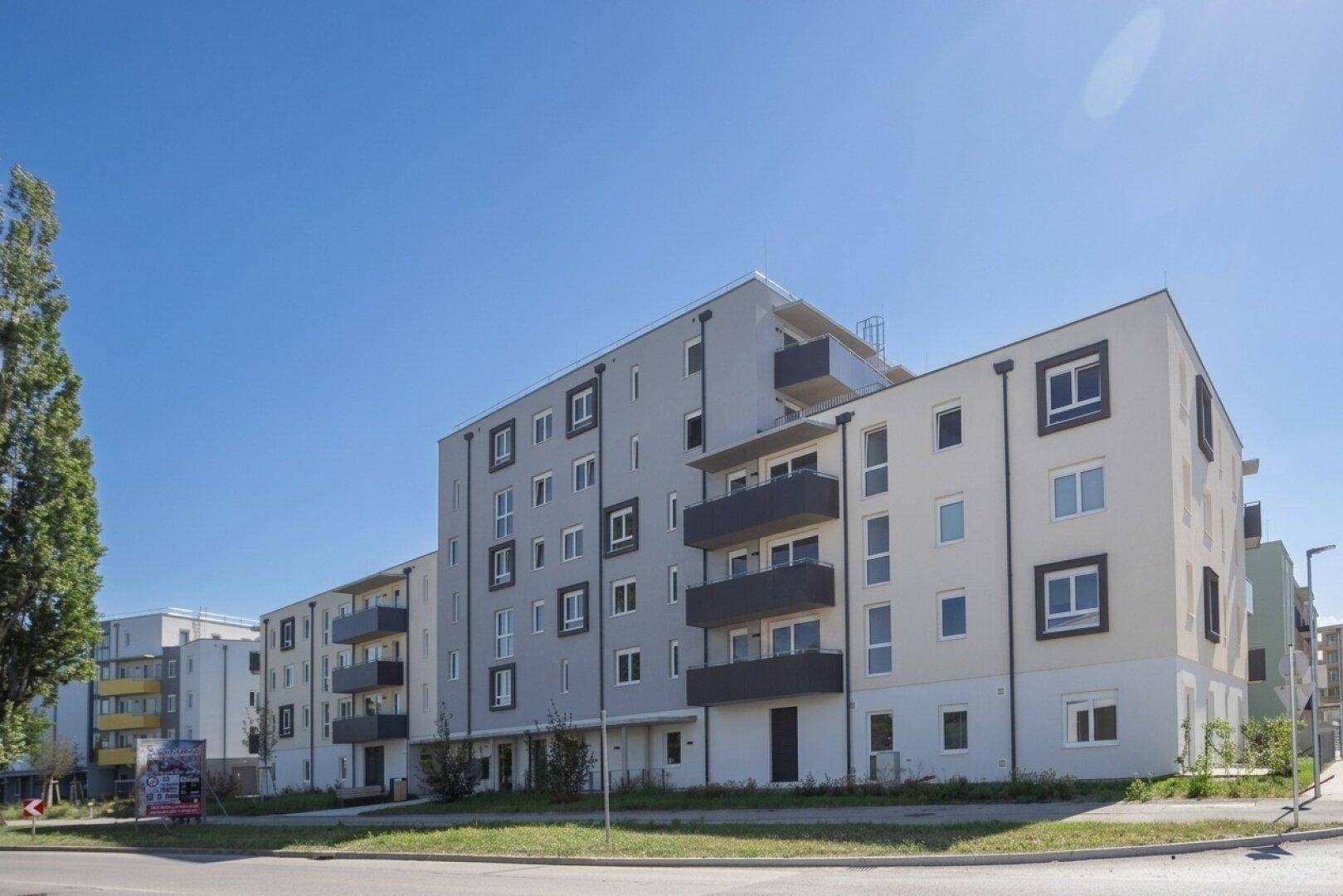 Neubau-Wohngebäude mit moderner Architektur, grauen und weißen Fassaden sowie Balkonen an einem sonnigen Tag.