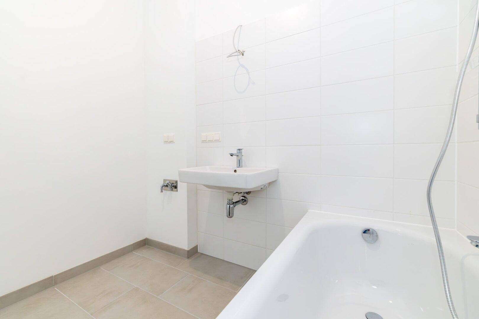 Funktionales Badezimmer mit weiß gefliesten Wänden, Badewanne und Waschbecken.