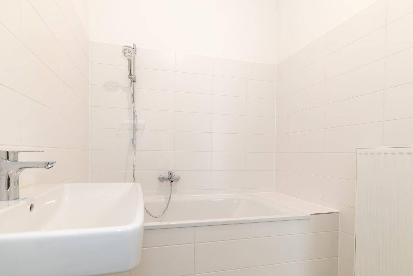 Helles Badezimmer mit weißer Badewanne, Duscharmatur und modernem Waschbecken.