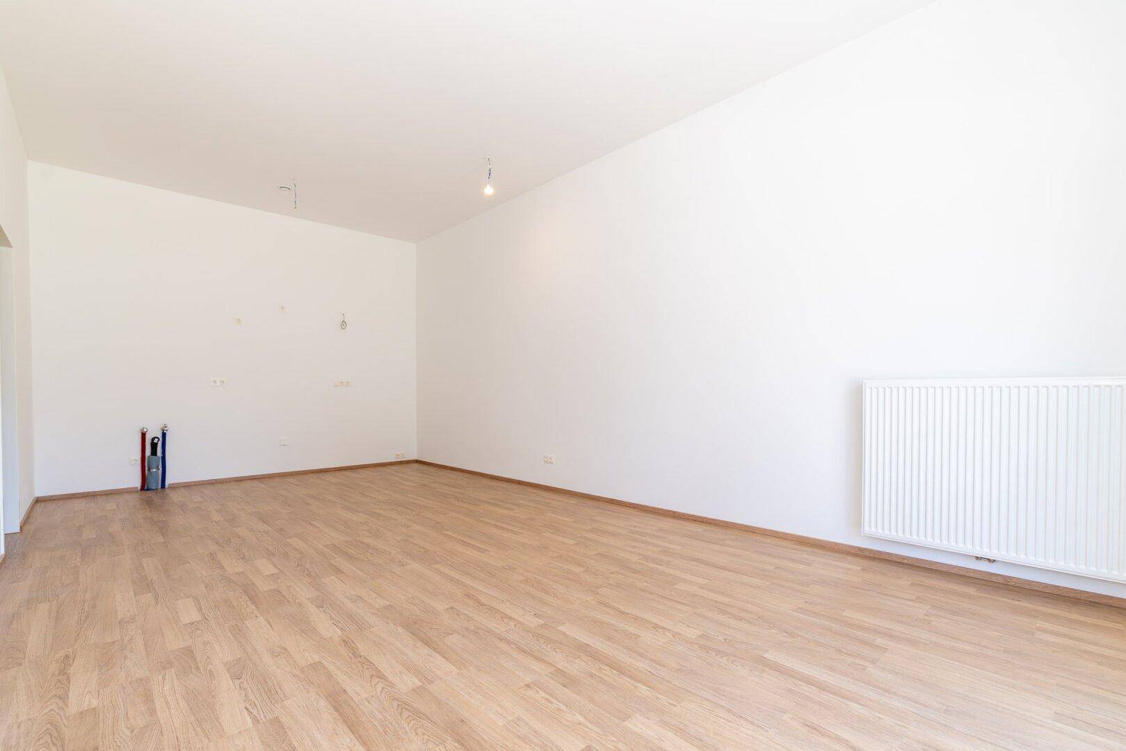 Leerer Wohnraum mit Laminatboden, Heizkörper und viel Potenzial zur individuellen Gestaltung.