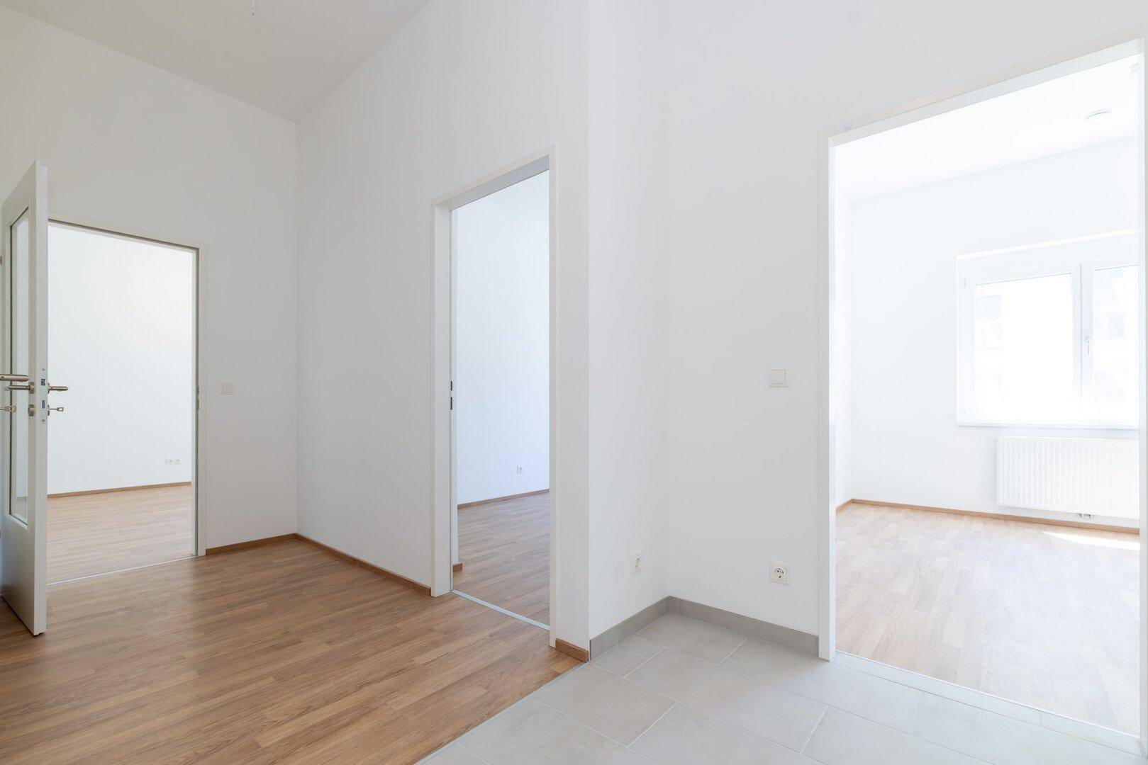 Geräumiger Flur mit Übergang von Laminat zu Fliesen und offenen Zugängen zu Zimmern.