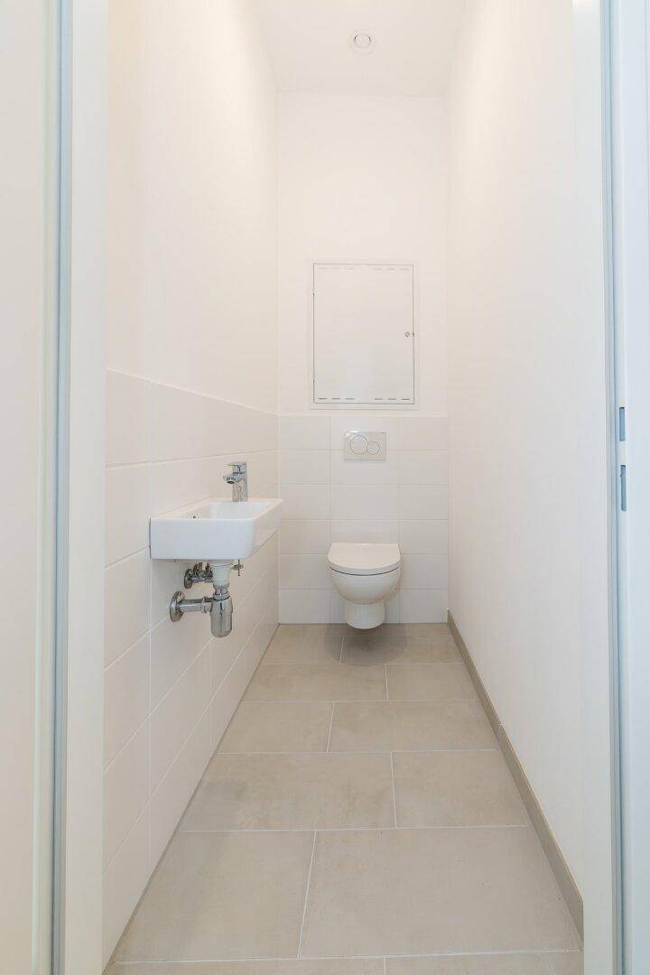 Separates Gäste-WC mit wandhängendem WC, kleinem Waschbecken und hellen Fliesen.