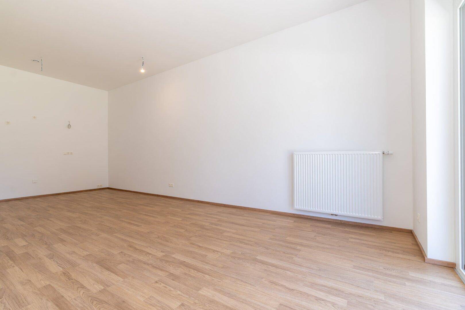 Heller Wohnbereich mit Laminatboden, weißer Wandgestaltung und großem Fenster zur Außenseite.
