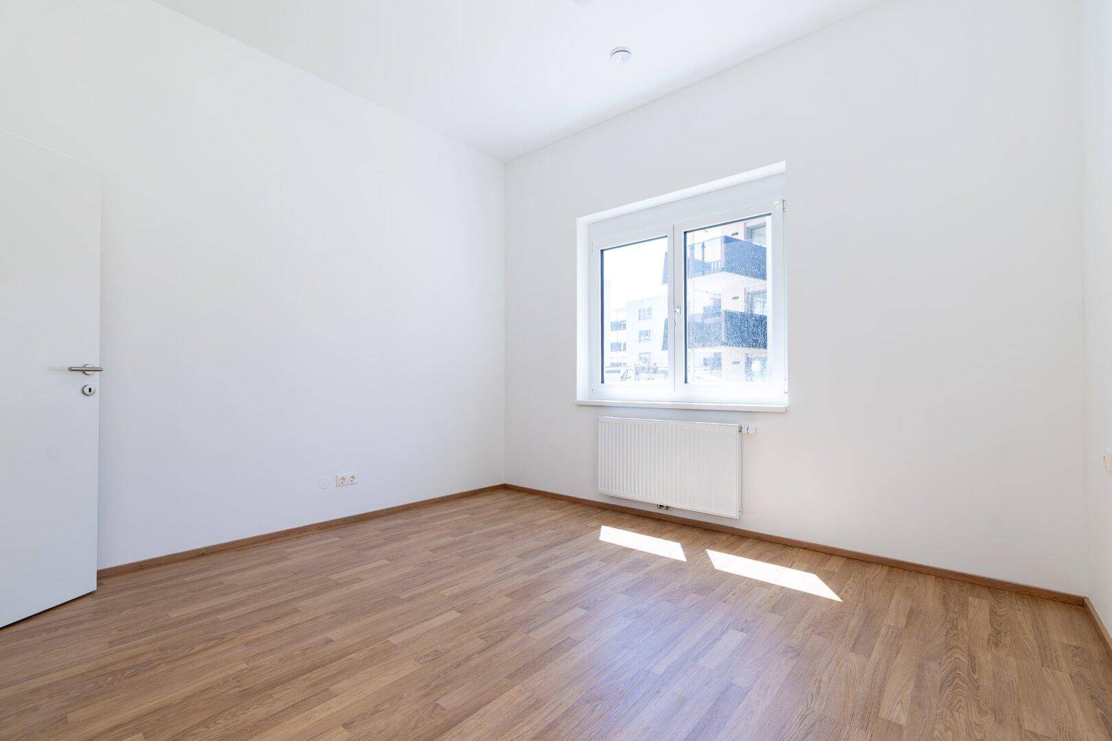 Unmöbliertes Schlafzimmer mit Laminatboden, weißer Wandfarbe und Blick nach draußen.