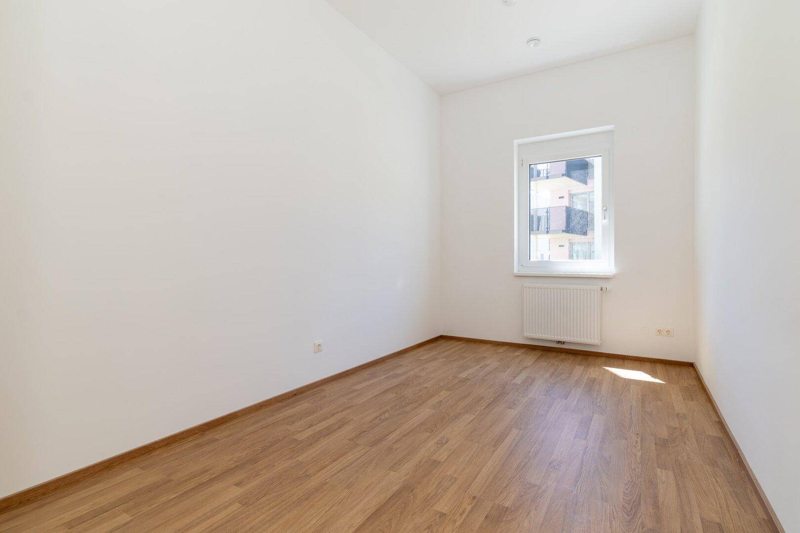 Helles Schlafzimmer mit Laminatboden, weiß gestrichenen Wänden und Fenster für Tageslicht.