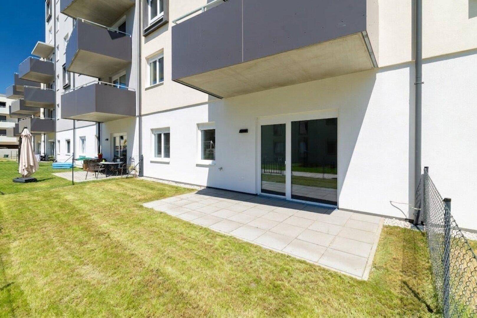 Sonnige Terrasse mit Rasenfläche und Blick auf weitere Wohngebäude im Hintergrund.