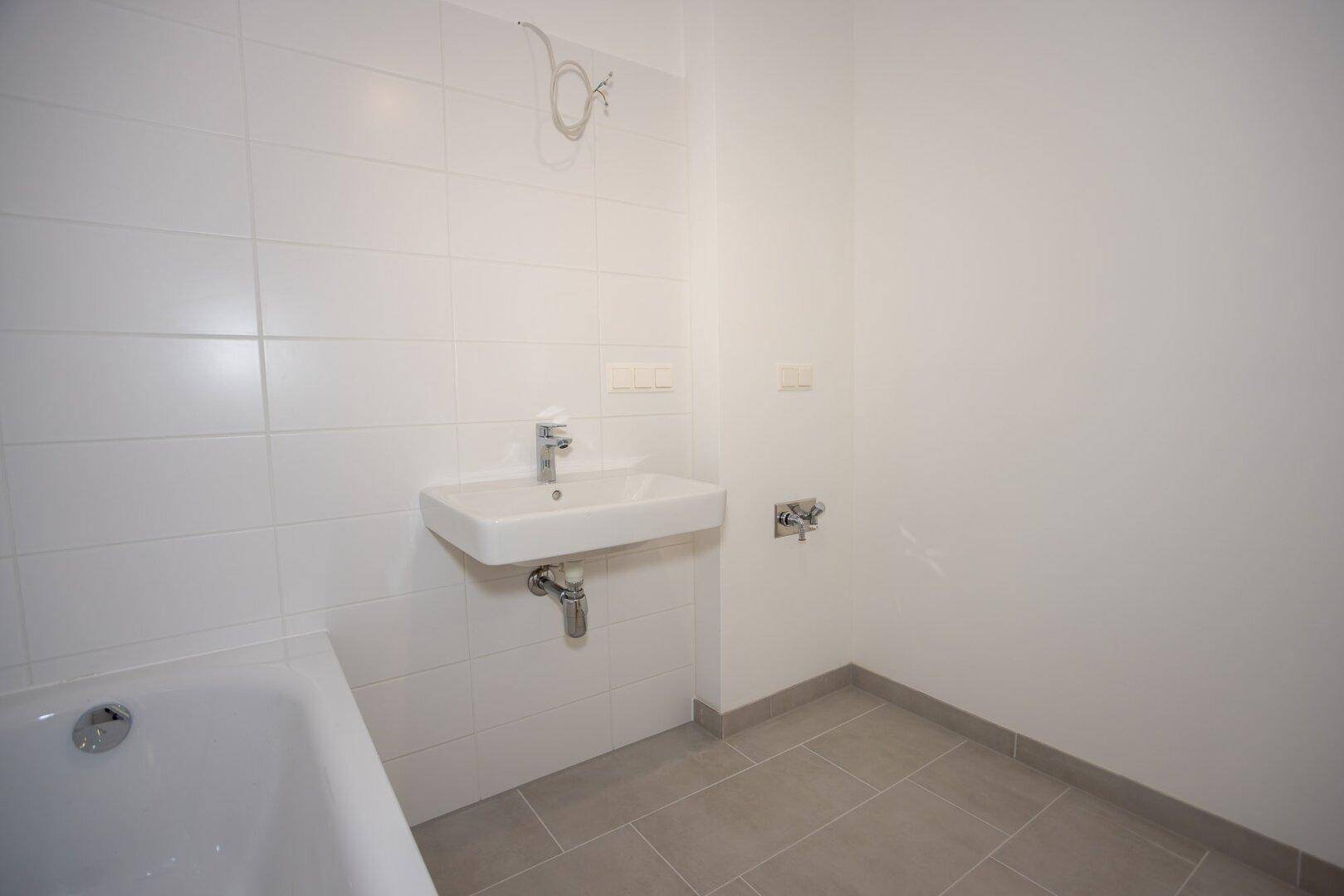 Helles Badezimmer mit Badewanne und Waschbecken, ausgestattet mit modernen Armaturen.