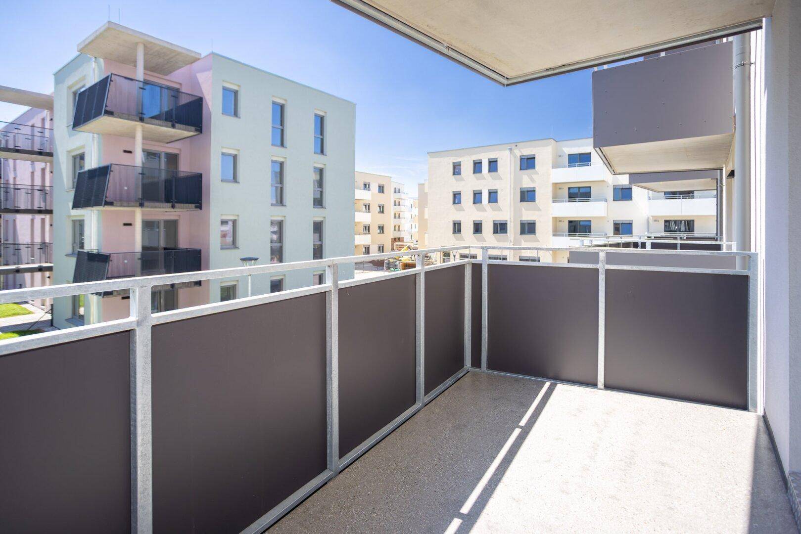 Moderner Balkon mit grauen Sichtschutzwänden und Blick auf die umliegenden Neubauten.
