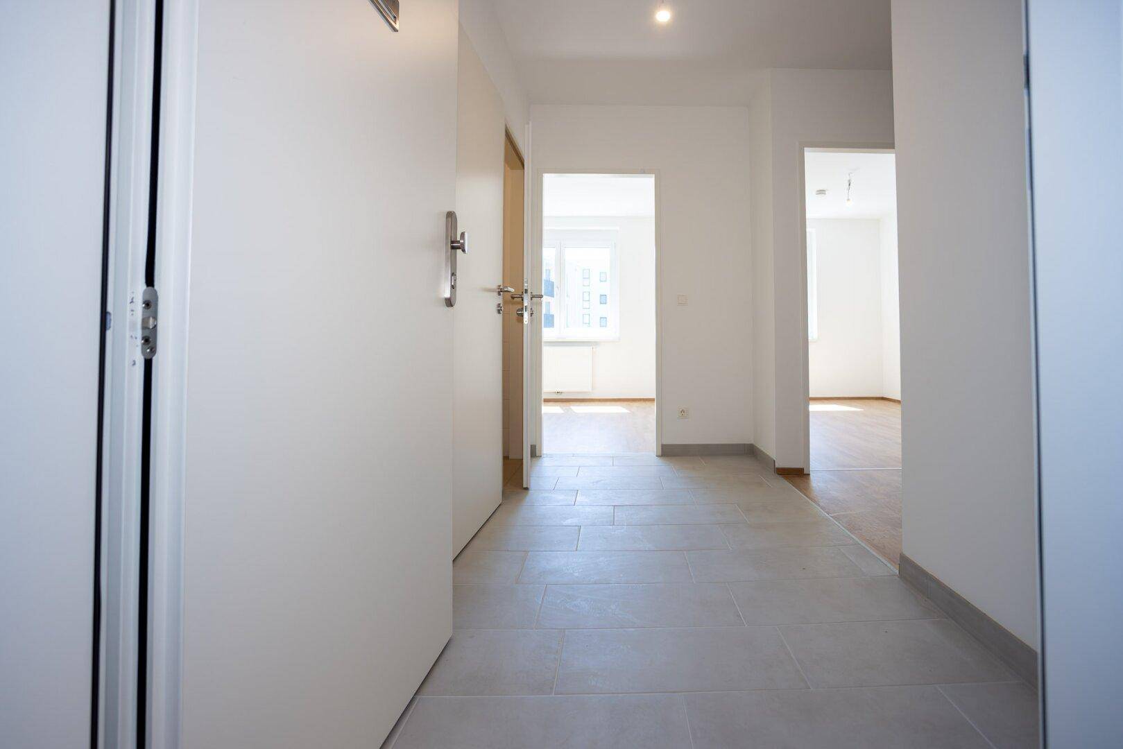 Heller Flur mit Fliesenboden, der zu verschiedenen Zimmern der Wohnung führt.