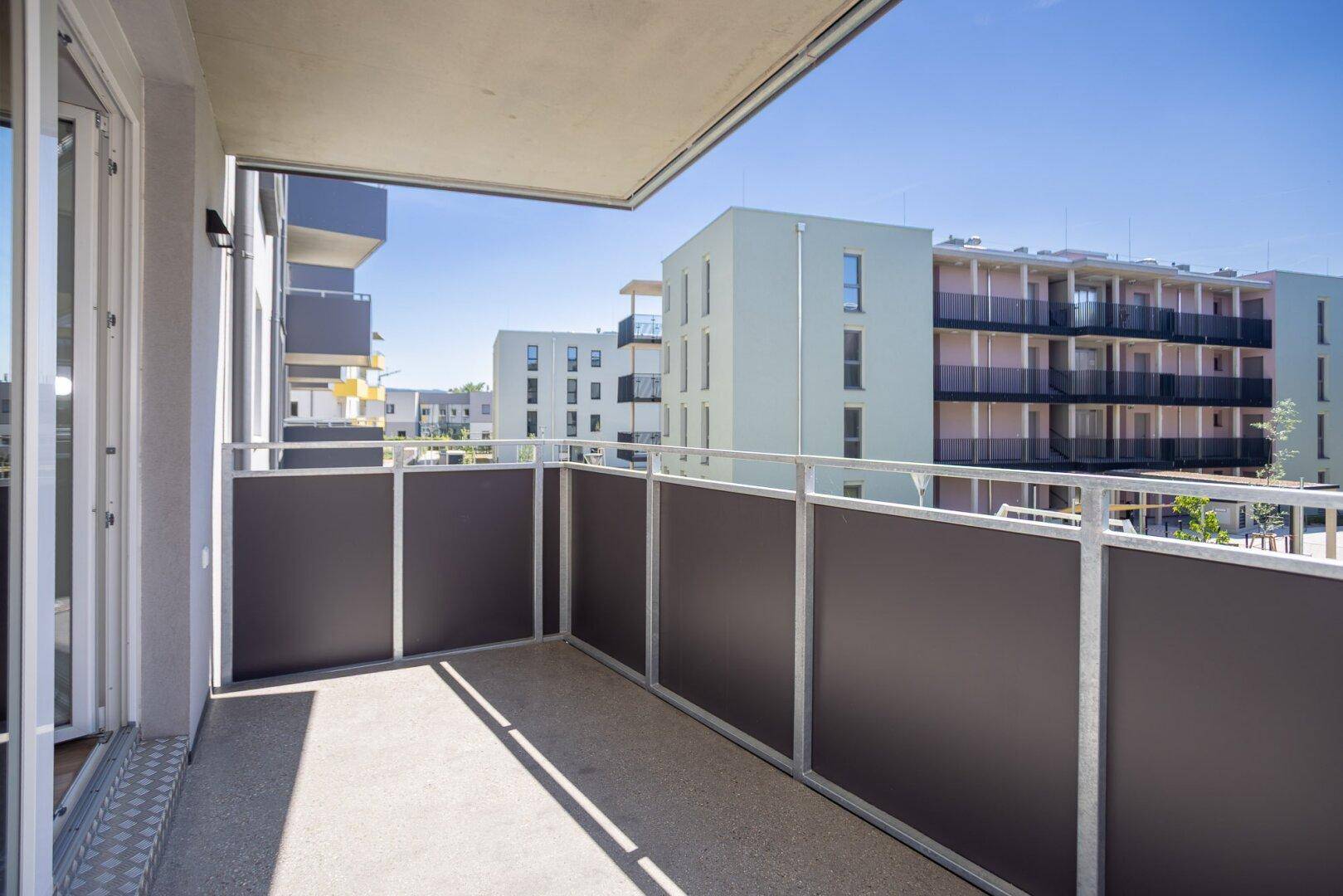 Geräumiger Balkon mit Blick auf die moderne Wohnanlage und viel Sonnenlicht.
